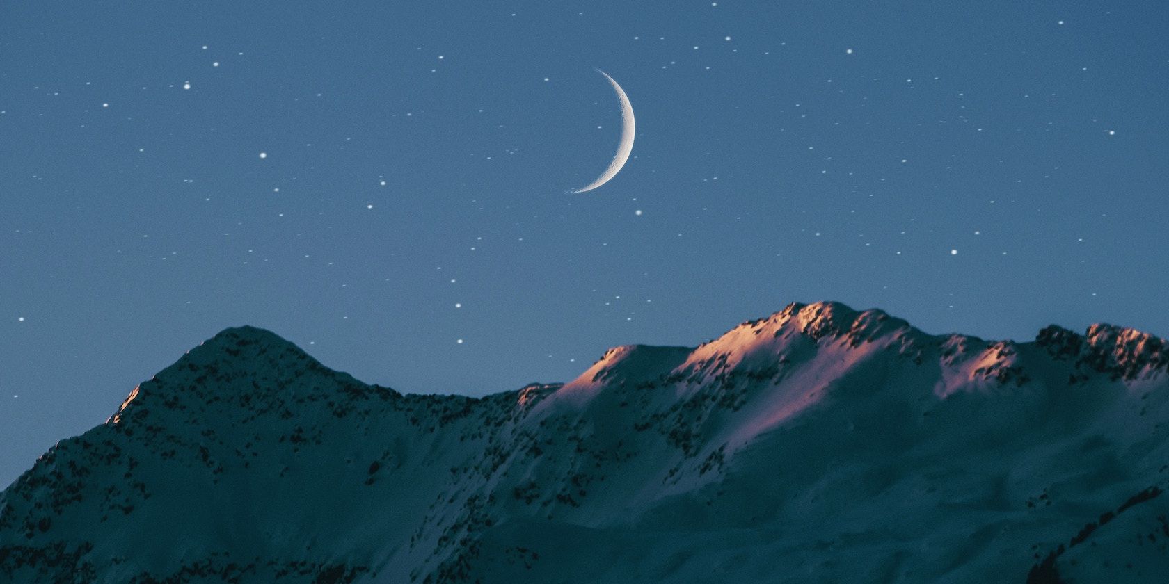A crescent moon over a mountain at nighttime