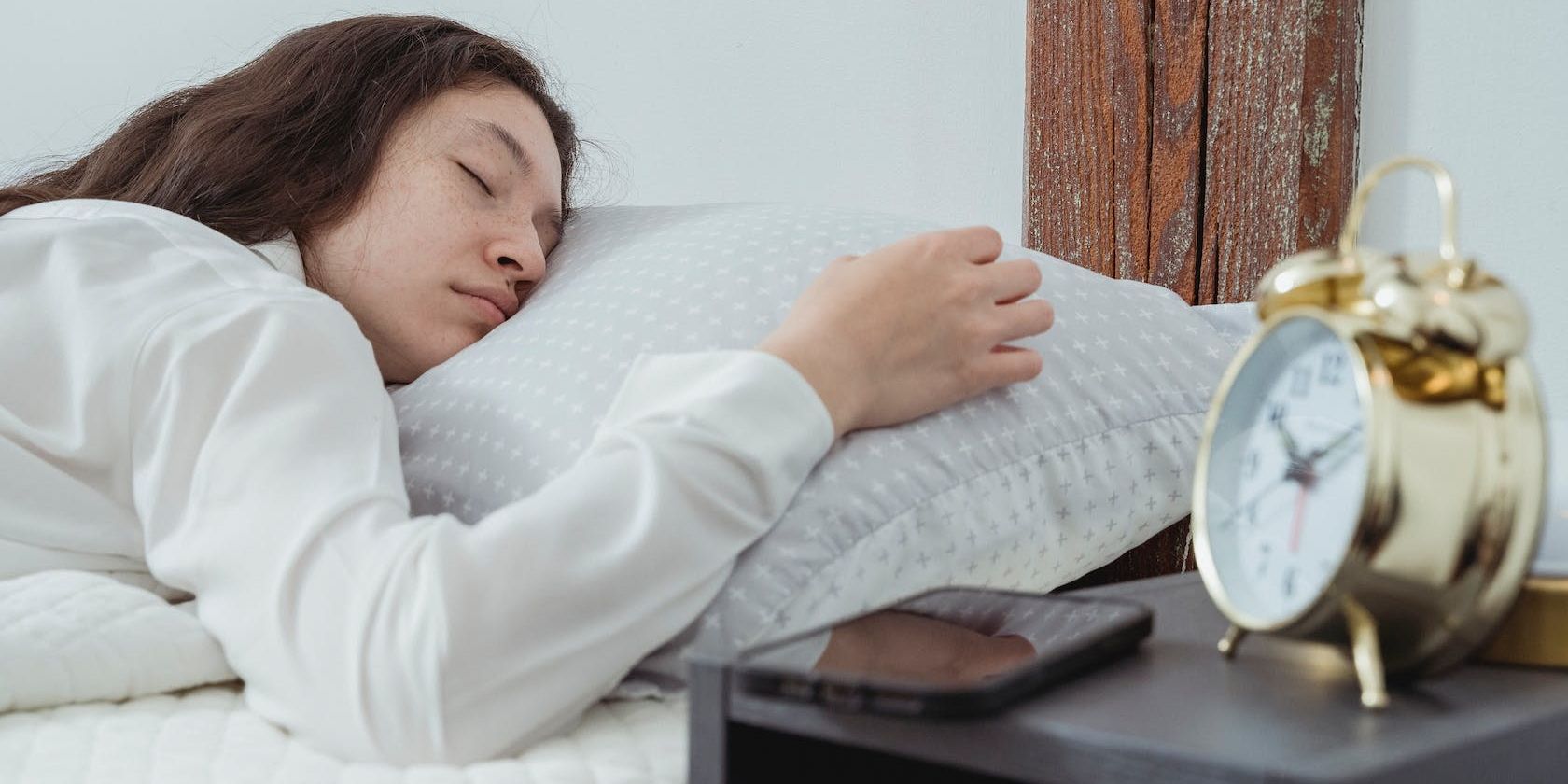 person sleeping next with a phone and clock on the nightstand