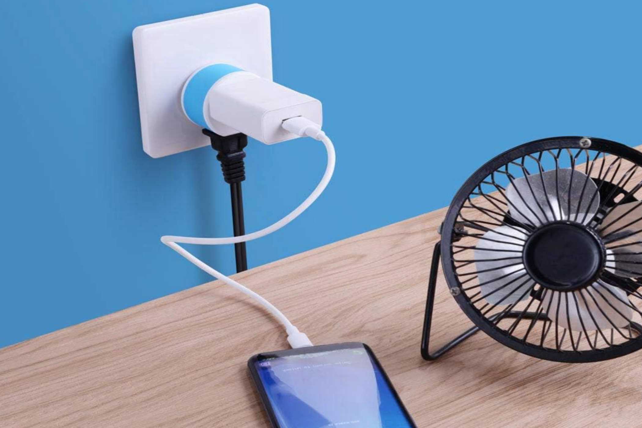 An OREI Full European Travel Adapter charging a smartphone and powering a small fan