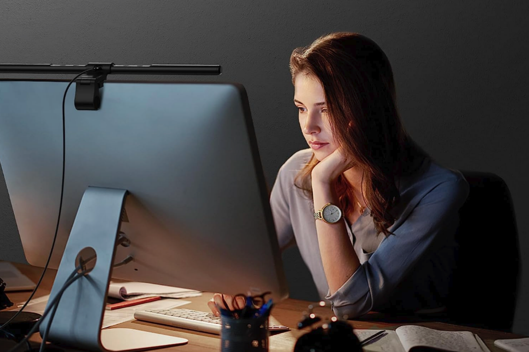 A woman using a monitor with a Quntis ScreenLinear Pro light bar attached on top.