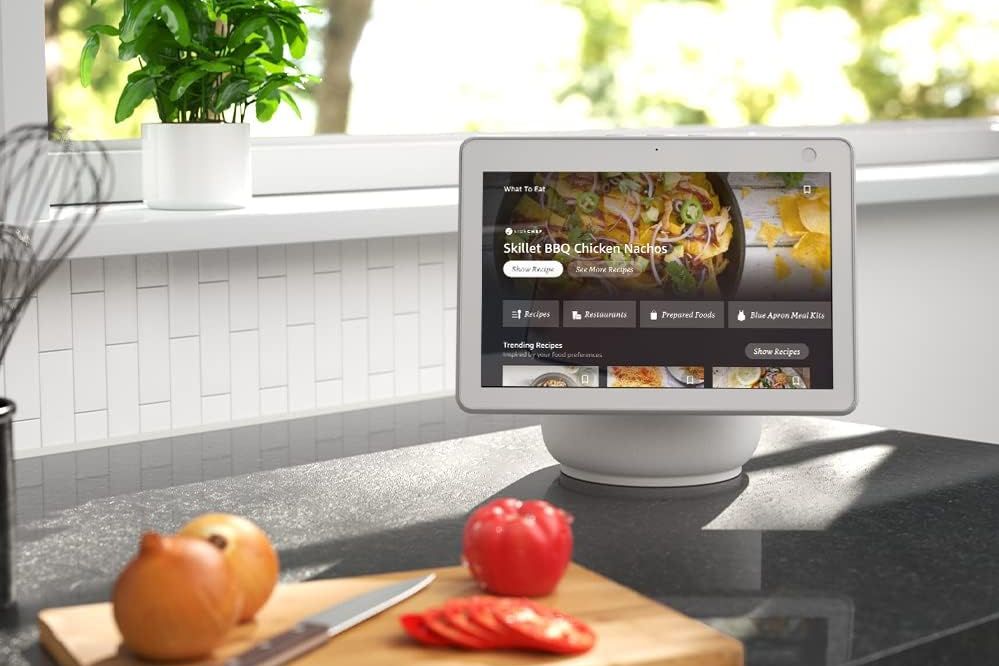 the amazon echo show 10 sits by a window in front of a cutting board