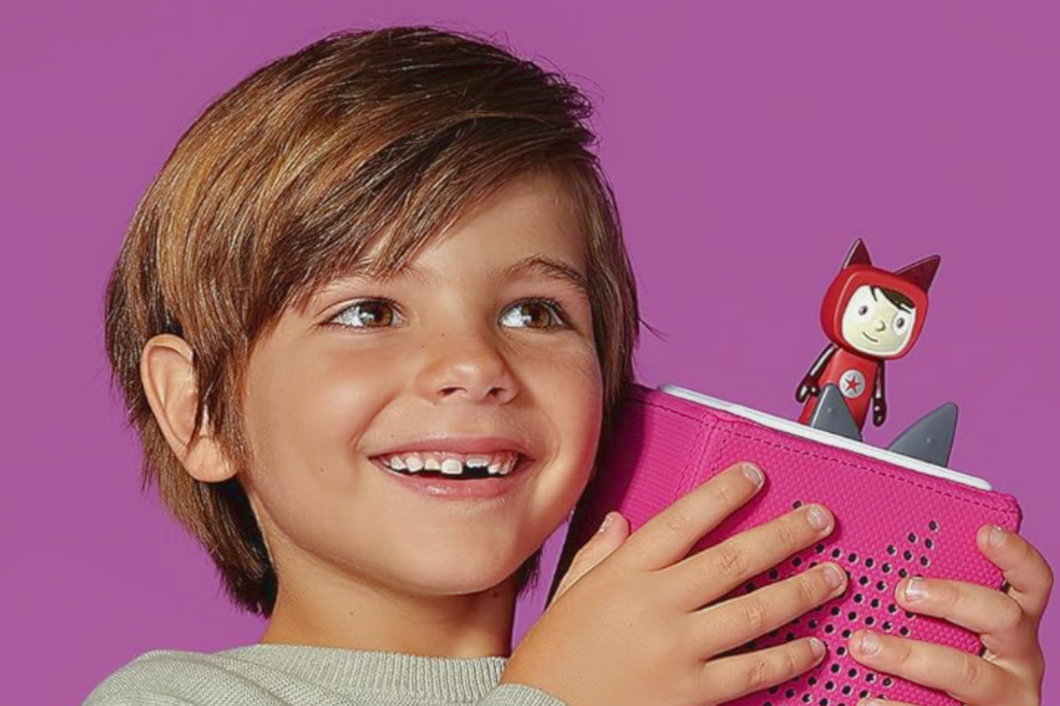 A young boy smiling and holding a Toniebox Audio Player Starter Set