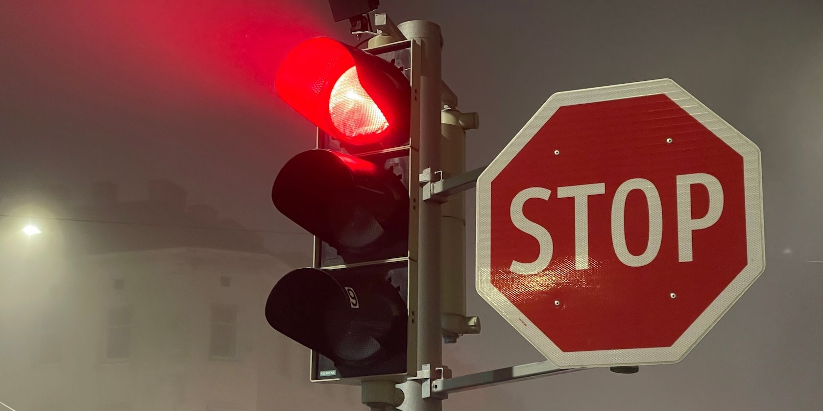 A set of traffic lights showing a red light next to a “STOP” sign