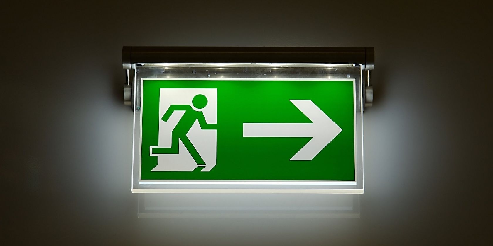 A green and white exit sign shows a stick figure leaving through a door with a large arrow pointing to the right.