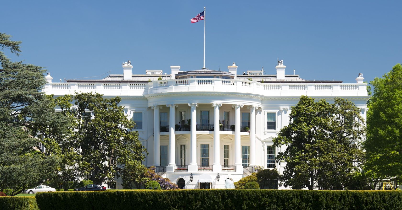 The White House, a wide white building with tall windows, columns, and a US flag.