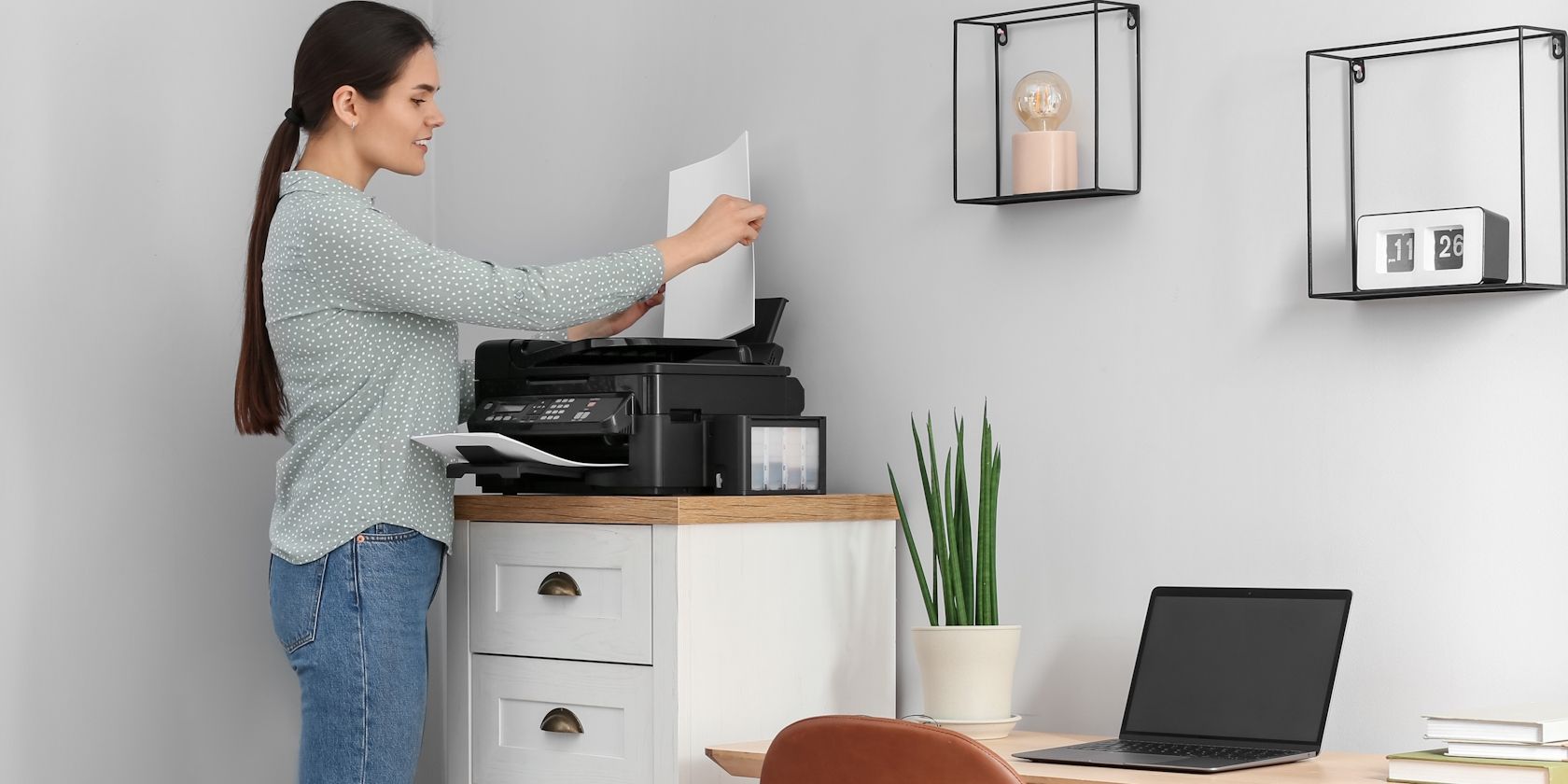 A woman using a printer with a MacBook on a desk