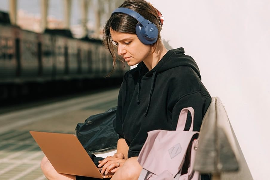 a woman wearing a jbl bluetooth headset types on her laptop