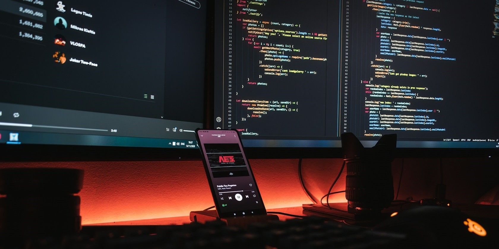 A workstation with two monitors and a mobile phone. A music player is open on the phone, while code is displayed on the two monitors.