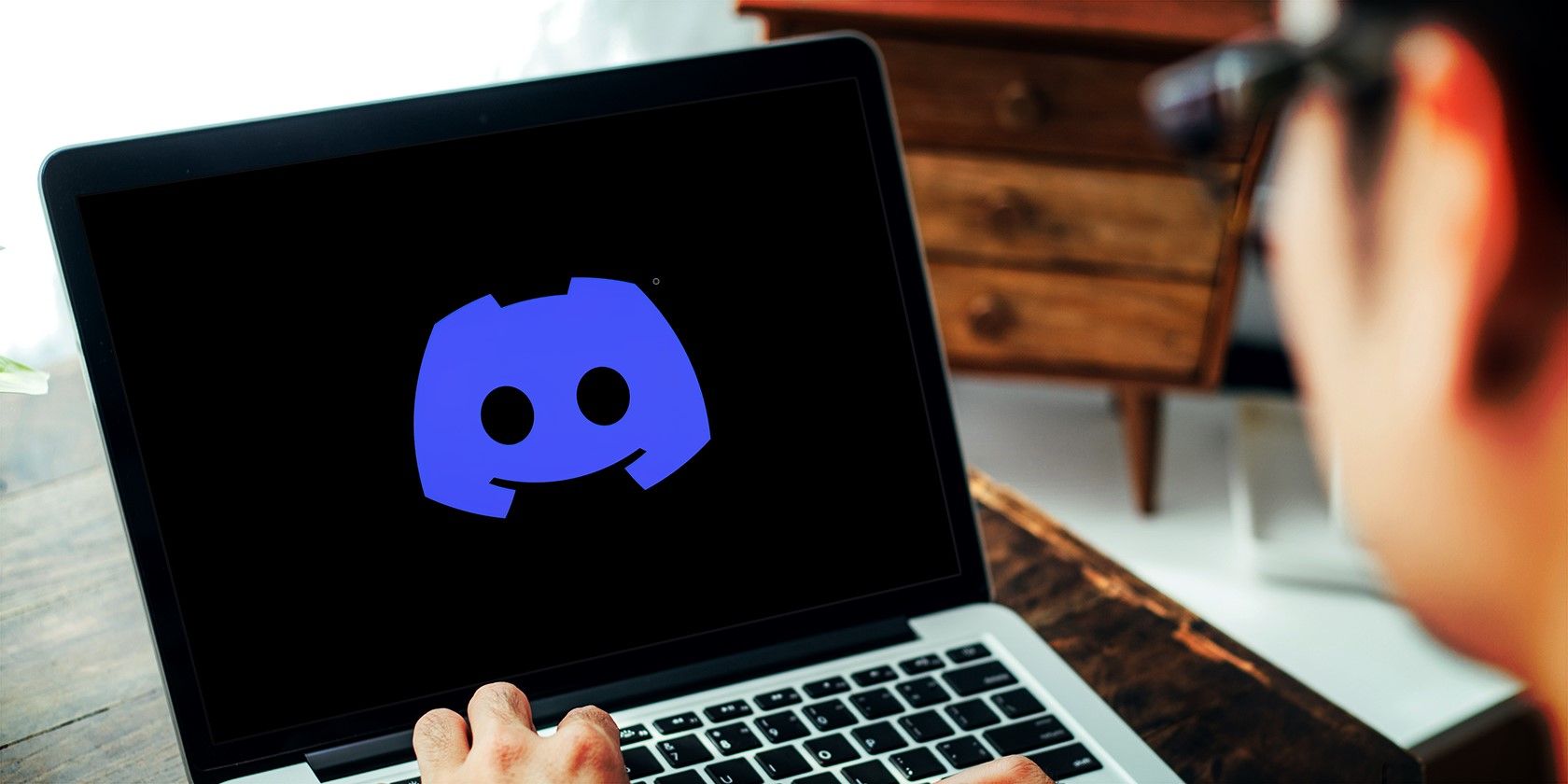 a person using a laptop with the Discord logo on the screen