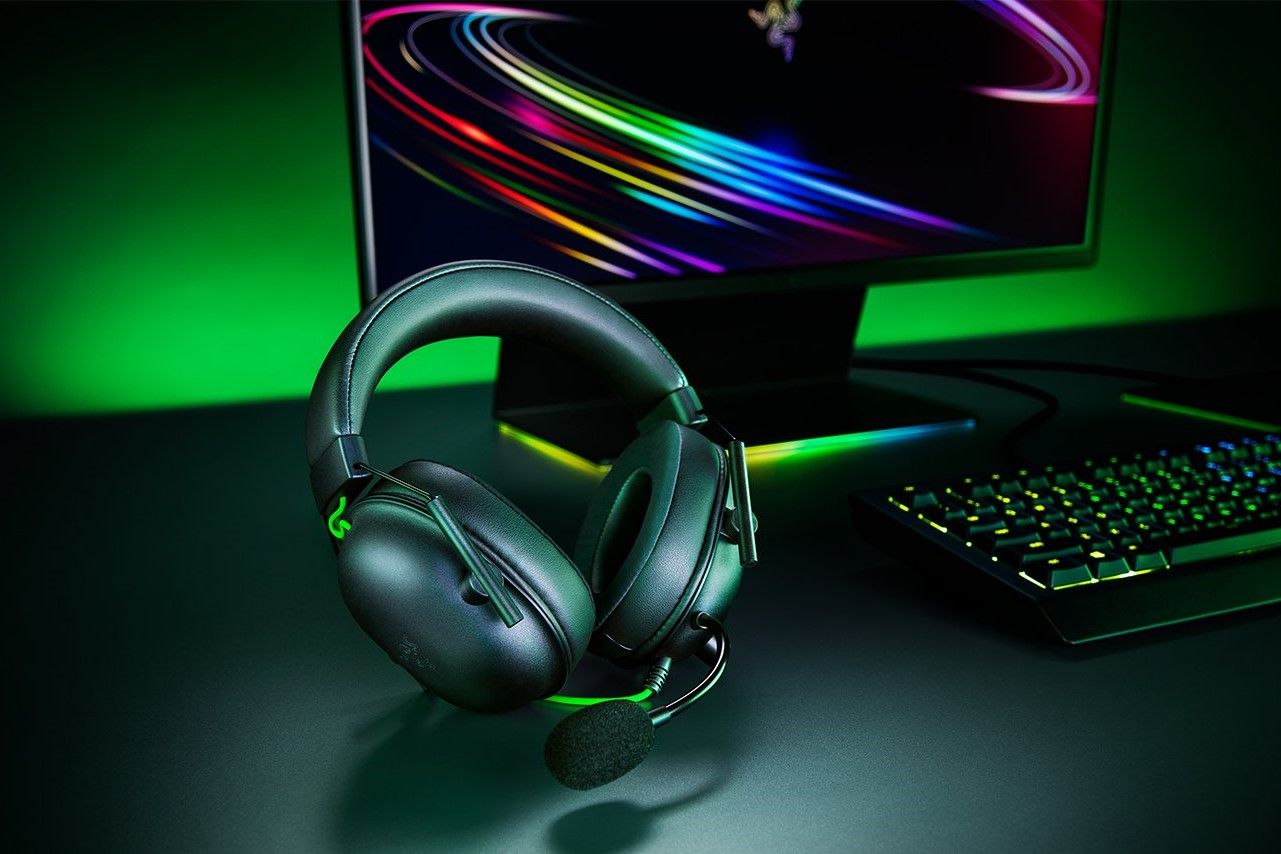 Razer Blackshark V2 X روی میزی در کنار کیبورد و مانیتور ریزر
