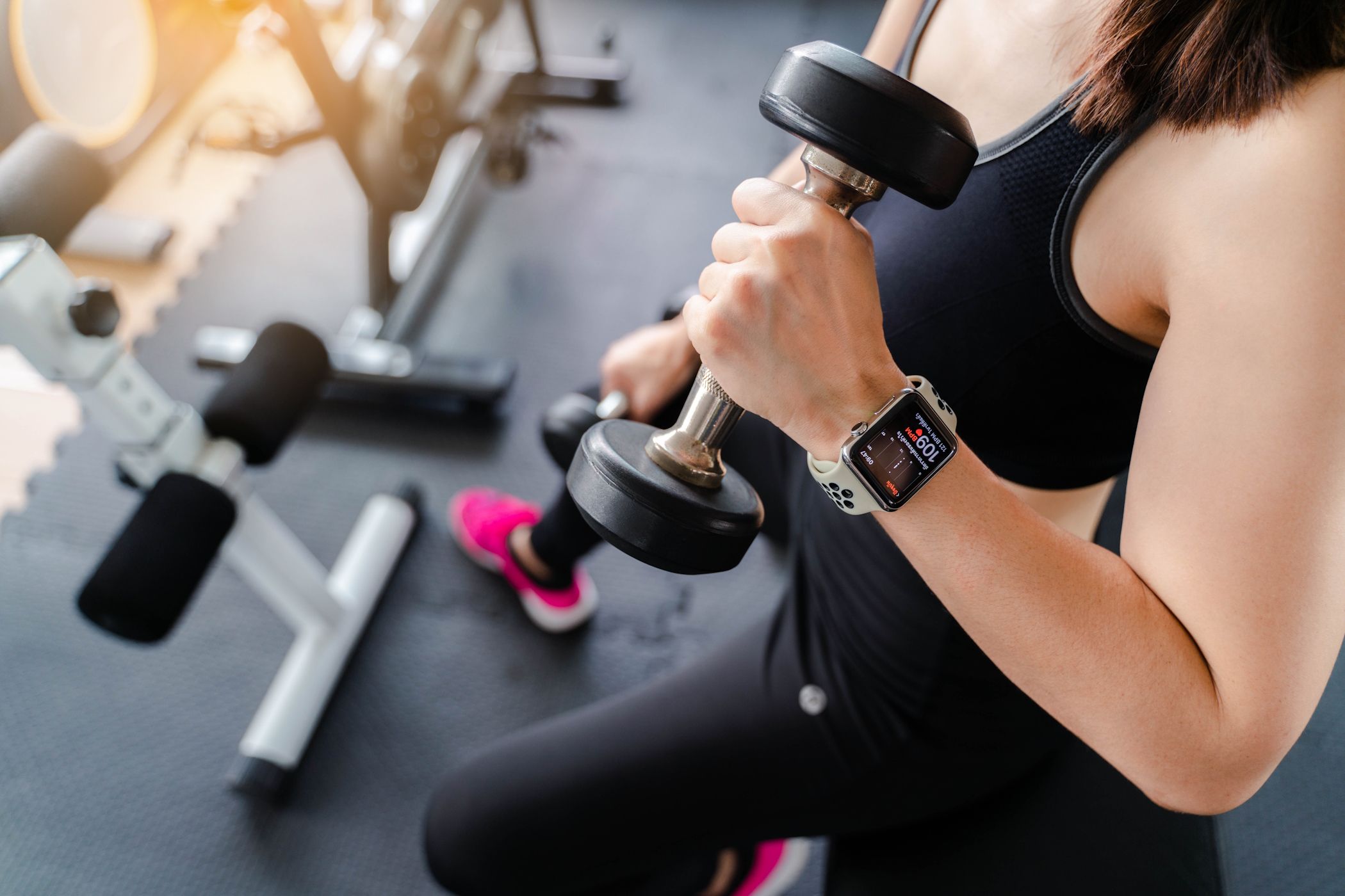 A woman lifting a dumbell at the gym wearing an Apple Watch in hand