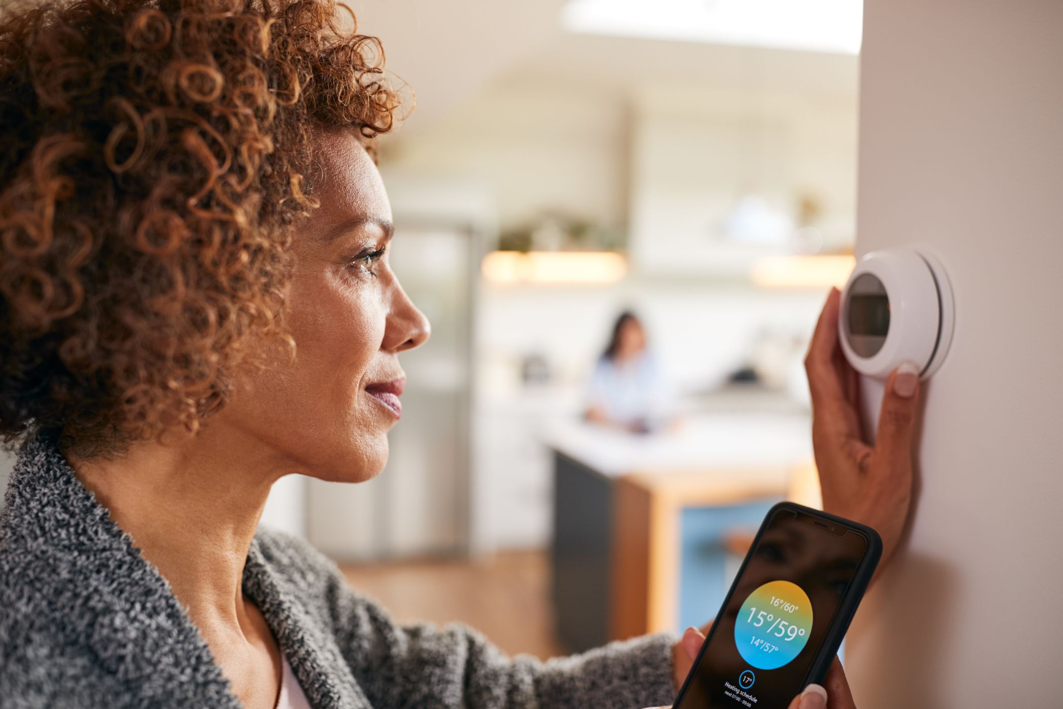 a woman using a smart thermostat with her smartphone
