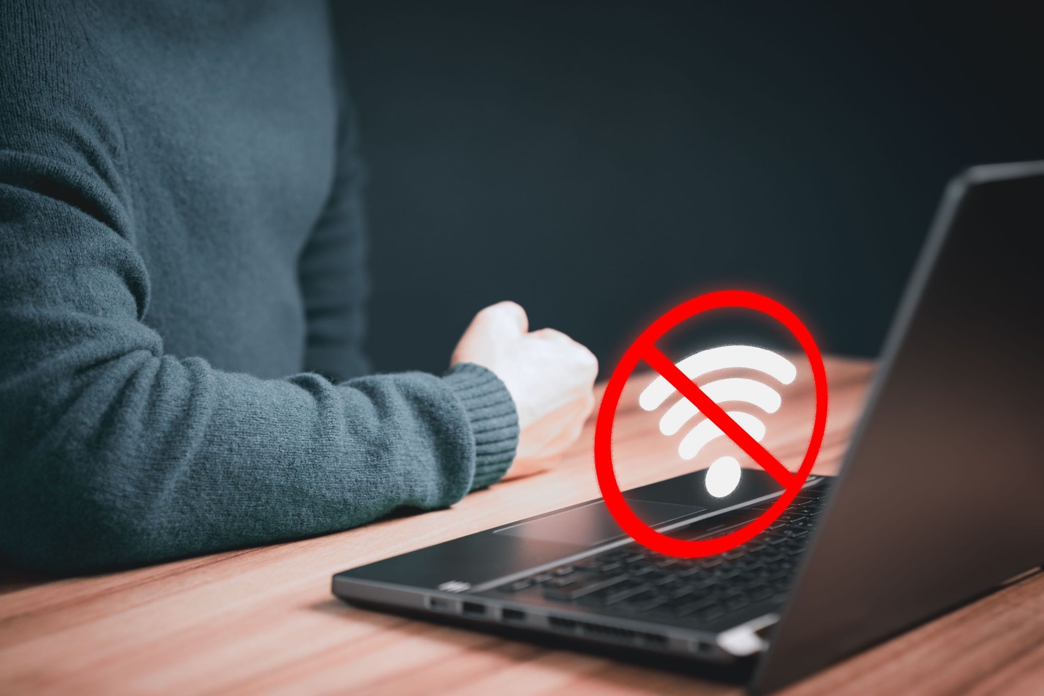 No Wi-Fi Connection icon above laptop with person's arm on table