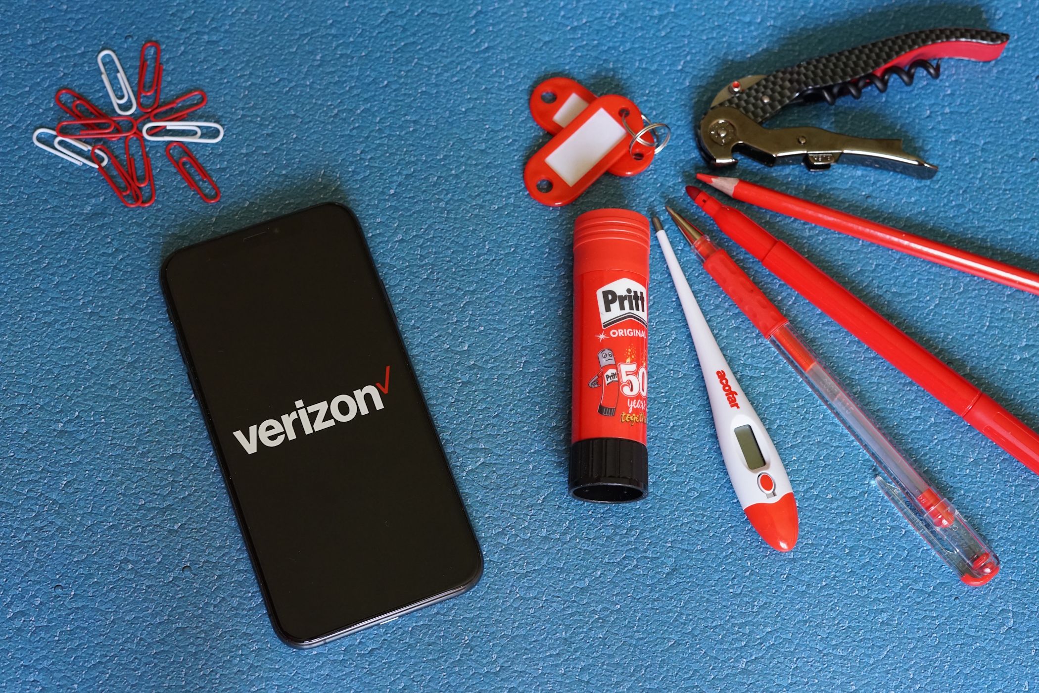 Verizon logo on an iPhone screen next to paper clips and red stationery