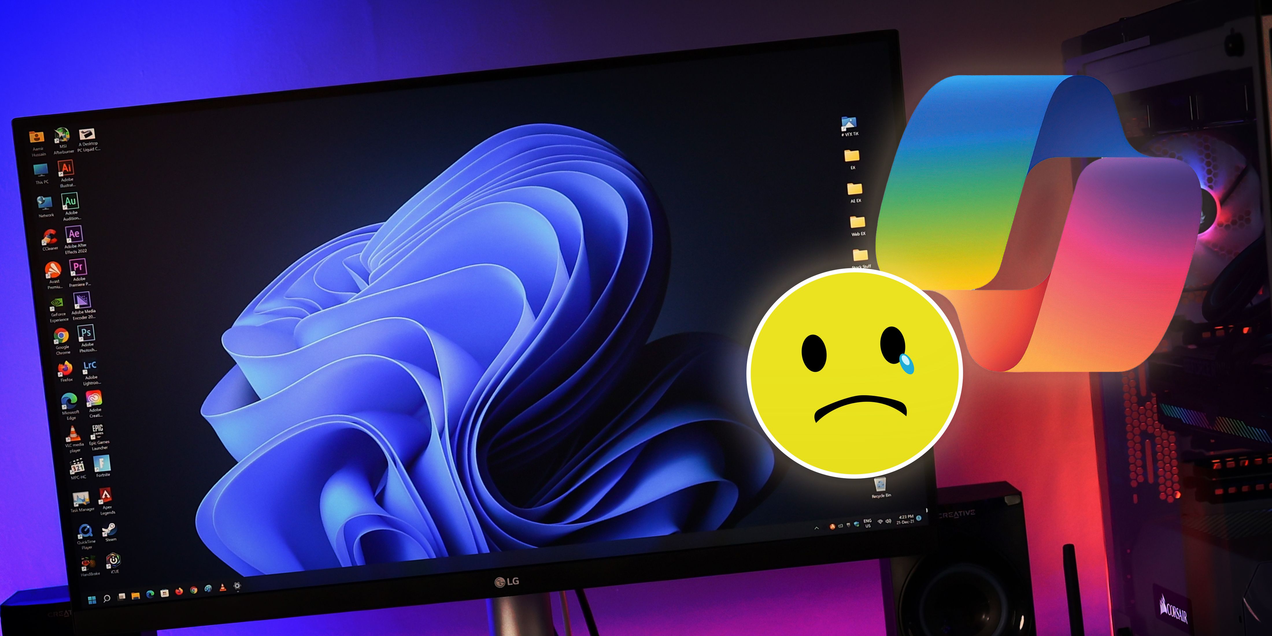A PC setup with a large monitor displaying Windows 11 wallpaper, accompanied by a sad emoticon icon