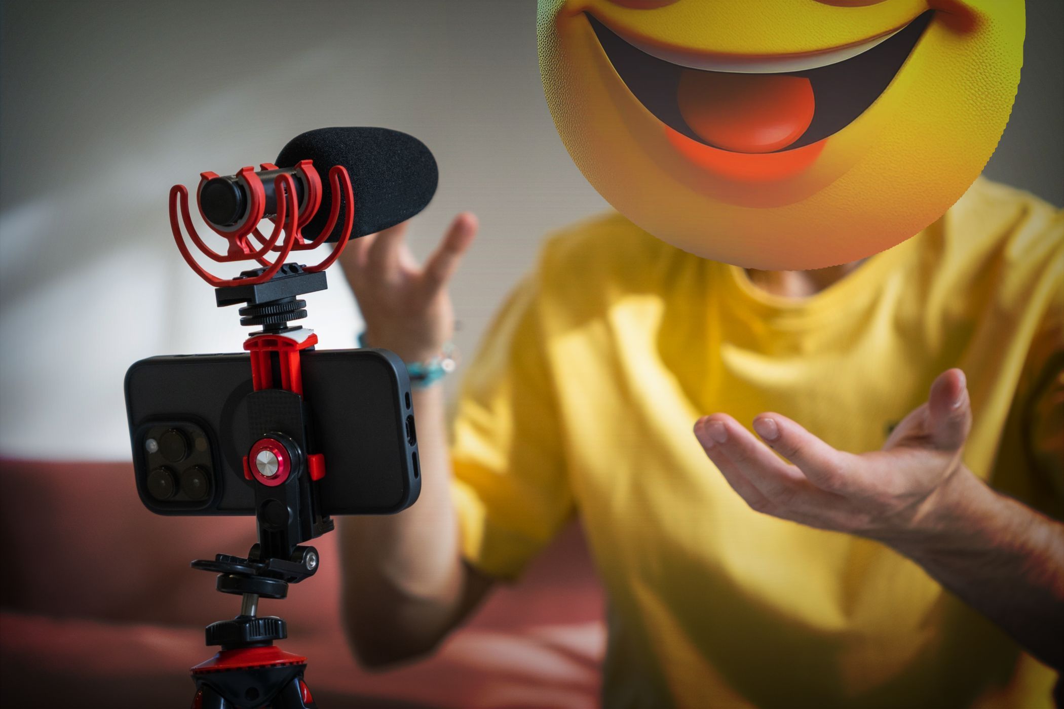 A person with a smiley face emoji head recording a video using a smartphone and microphone setup.