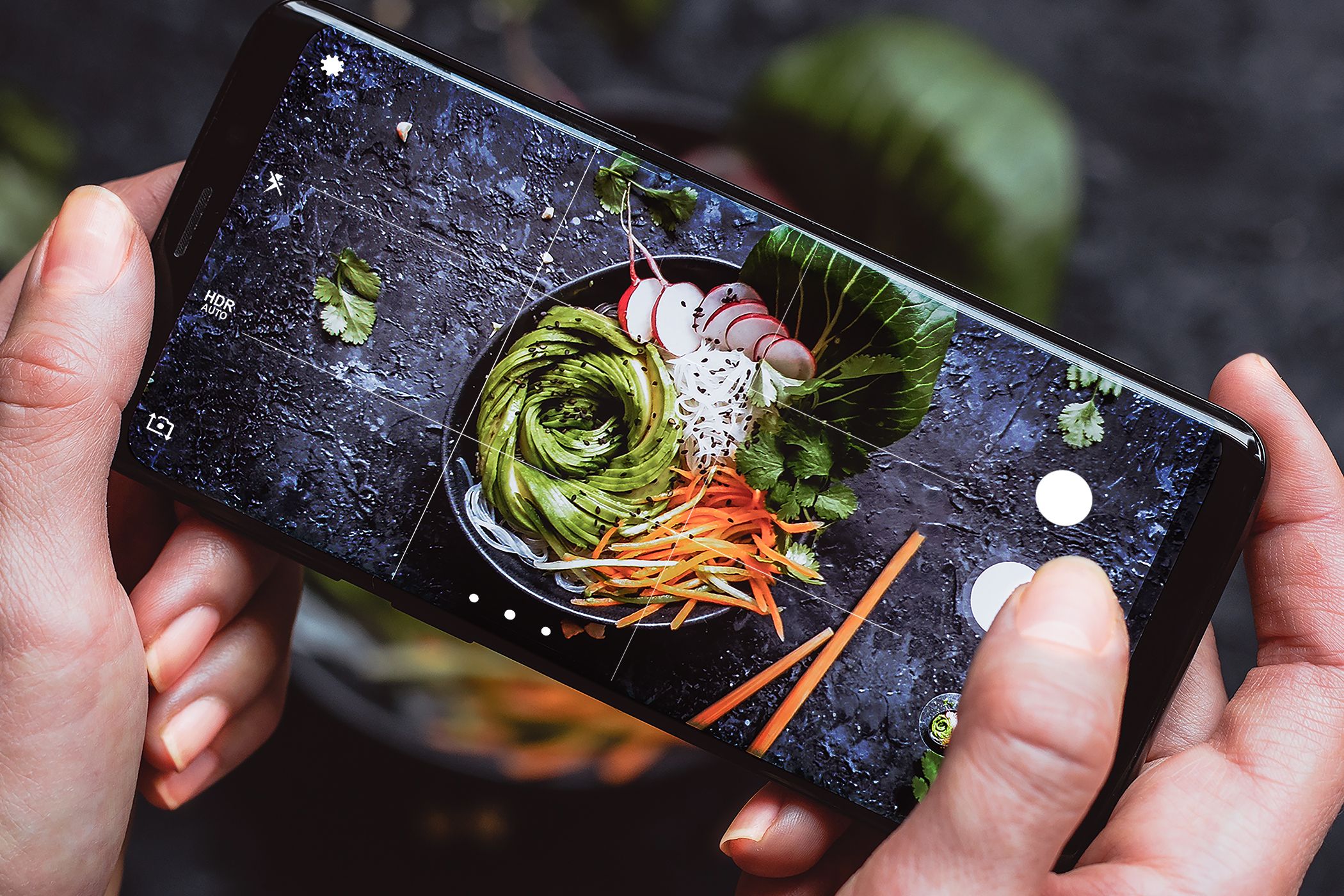 Person taking a photo of a beautifully plated salad with a smartphone, emphasizing food photography and culinary presentation.