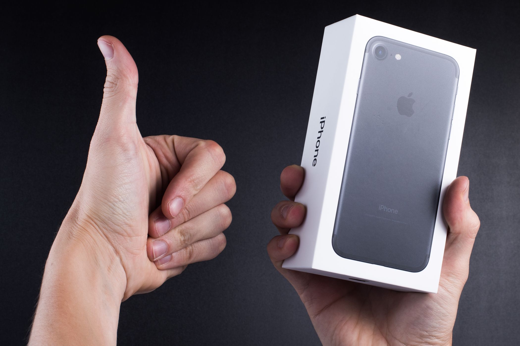 A man holding an iPhone box in one hand and giving a thumbs up