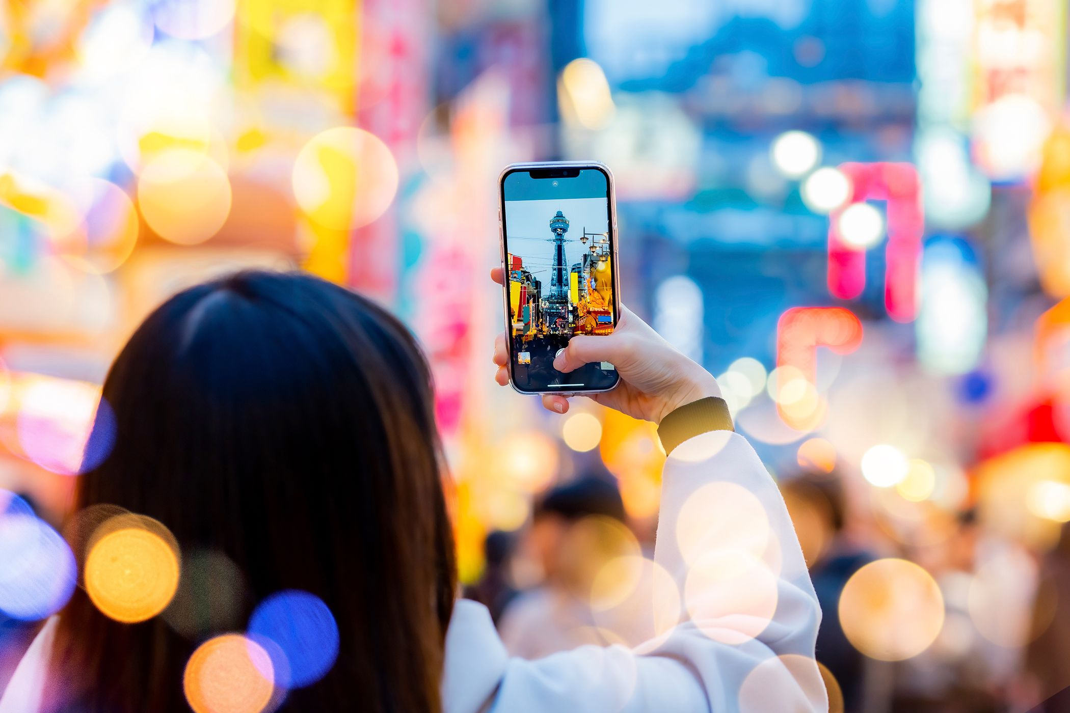 A woman taking a photo with her phone with a bokeh effect background.