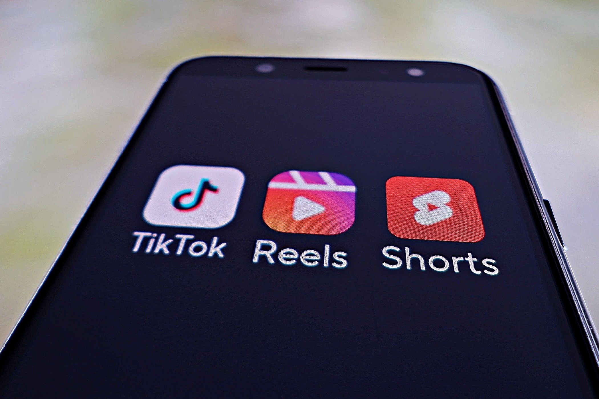 Smartphone displaying icons for TikTok, Instagram Reels, and YouTube Shorts