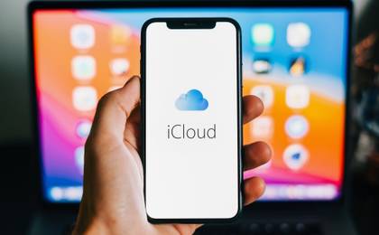 iCloud logo appearing on an iPhone with a MacBook in the background