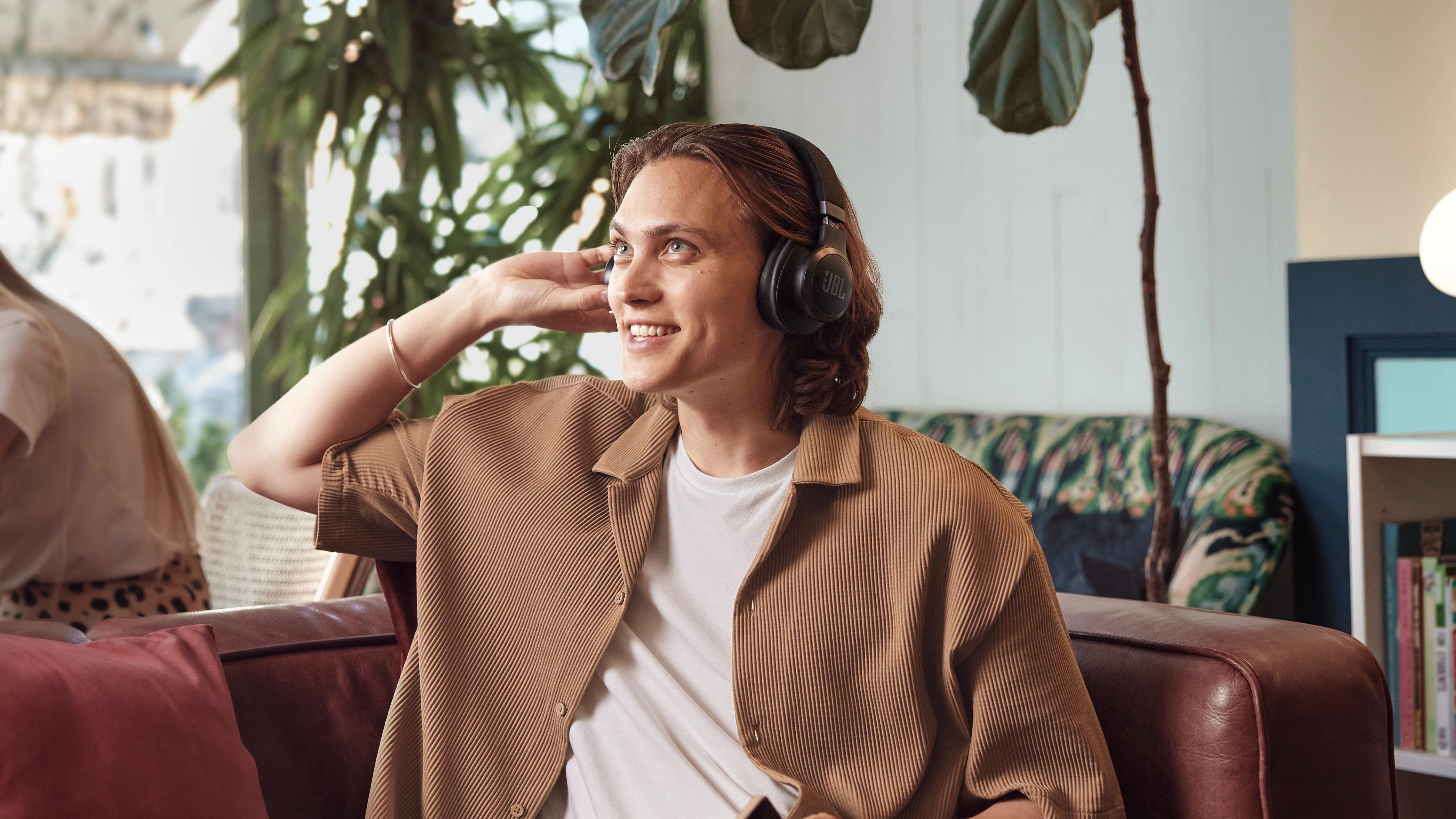 A person sitting on a couch wearing JBL LIVE 770NC headphones