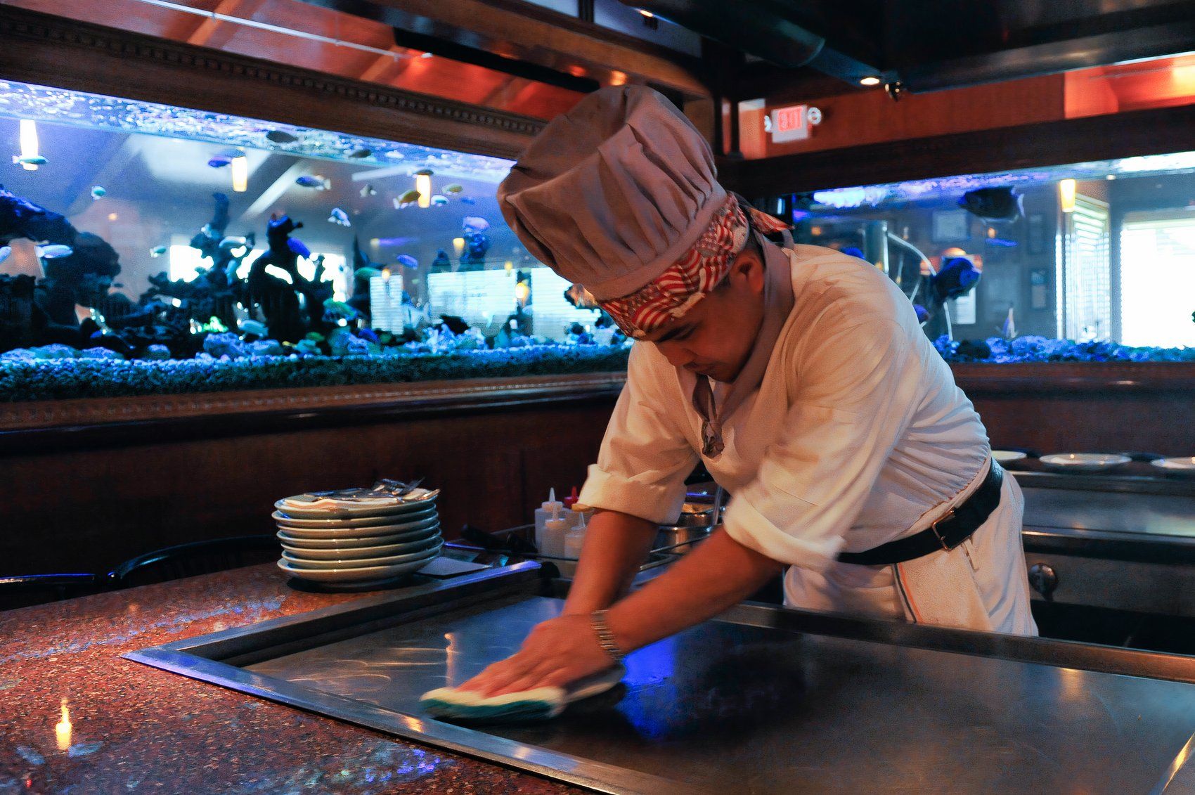 Man in chef's outfit wiping down a hibachi grill 