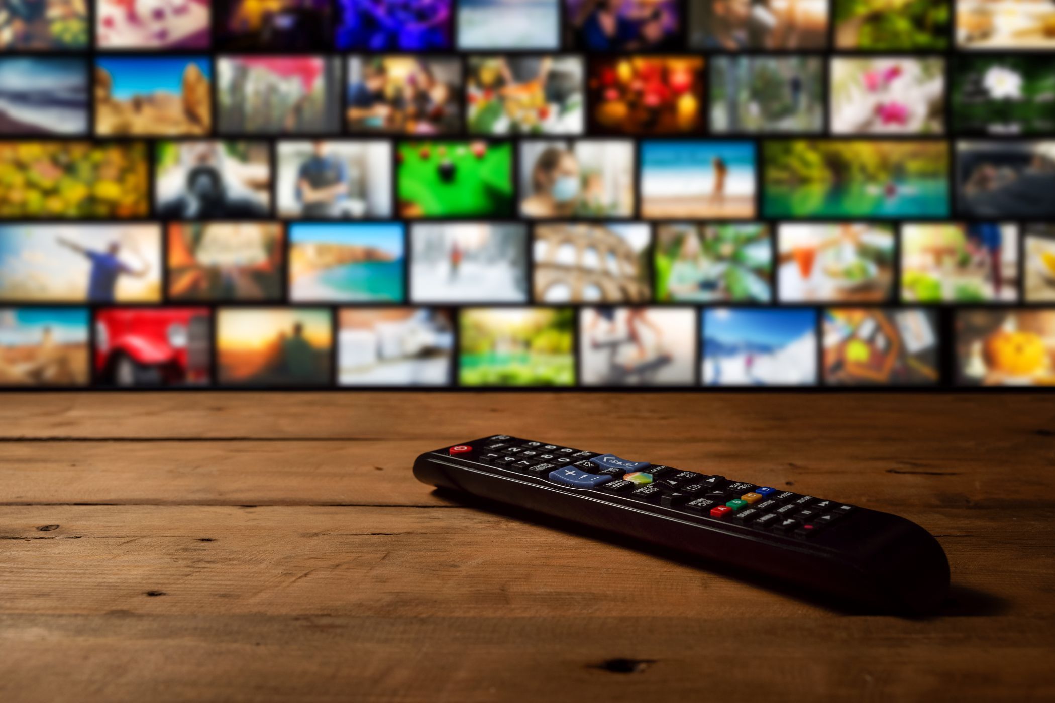 a close-up of a TV remote control with a TV screen in the background