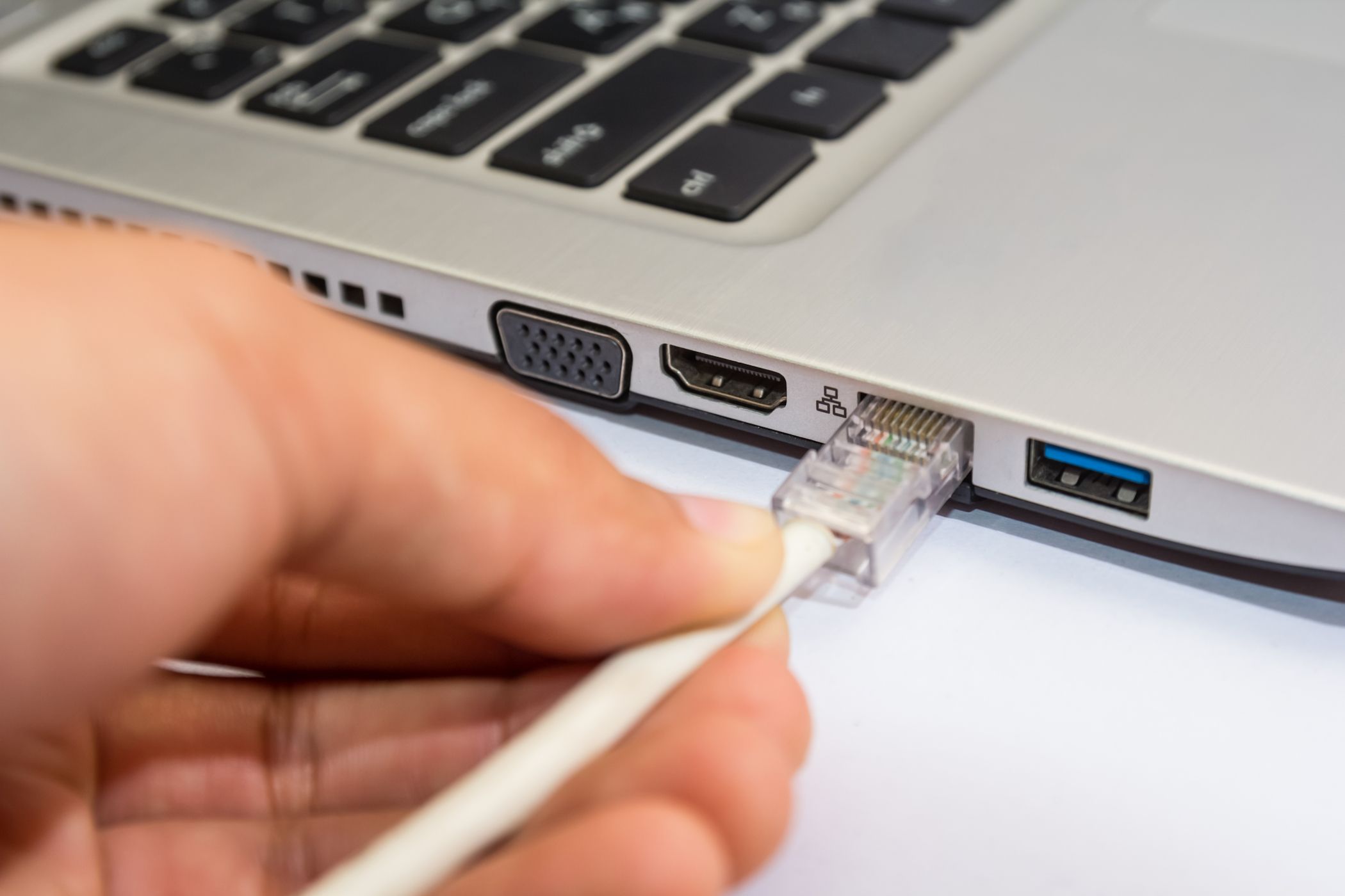 A man connecting an Ethernet cable to a Windows laptop