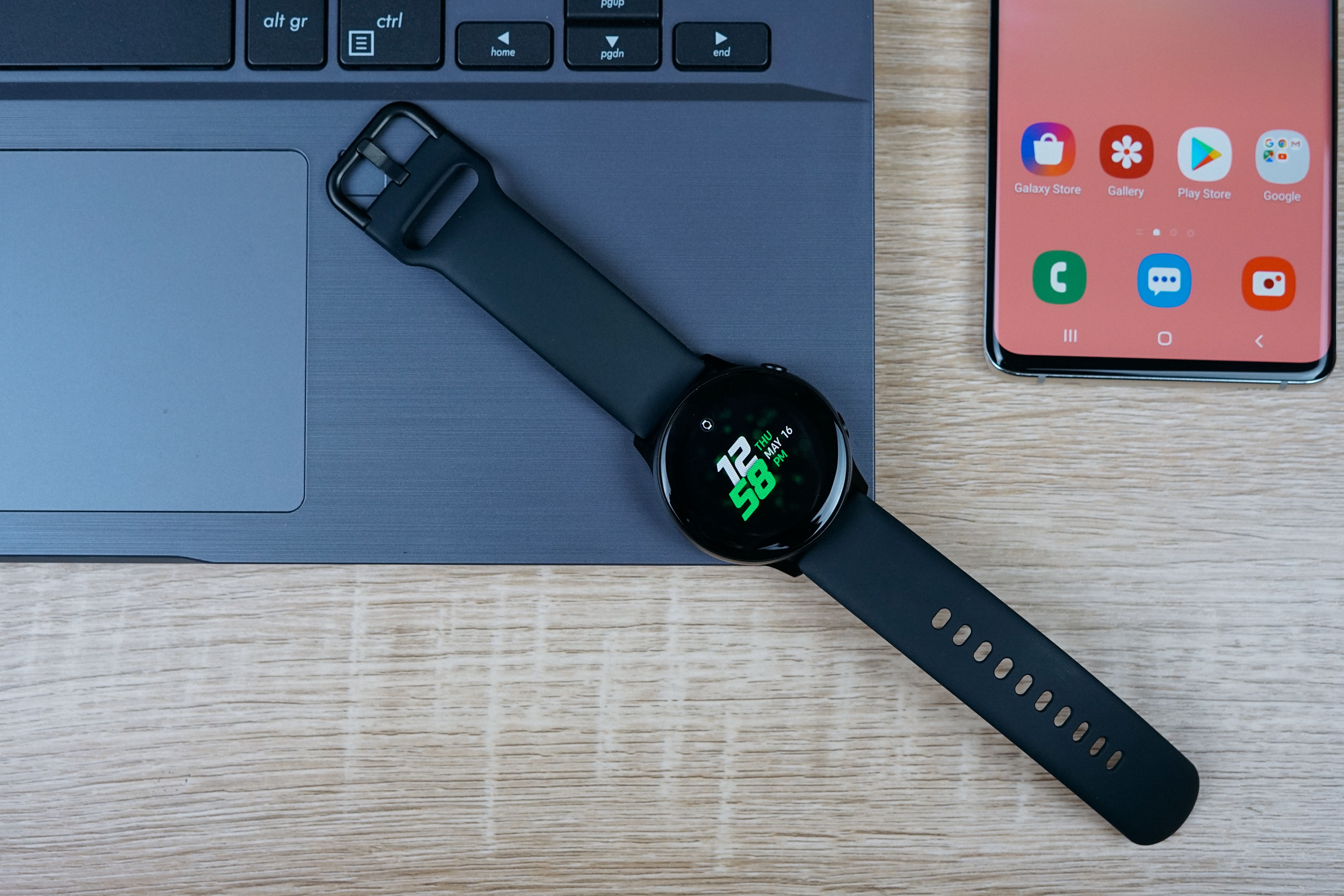 Samsung Galaxy Watch Active next to a Galaxy S10 and a laptop on a desk