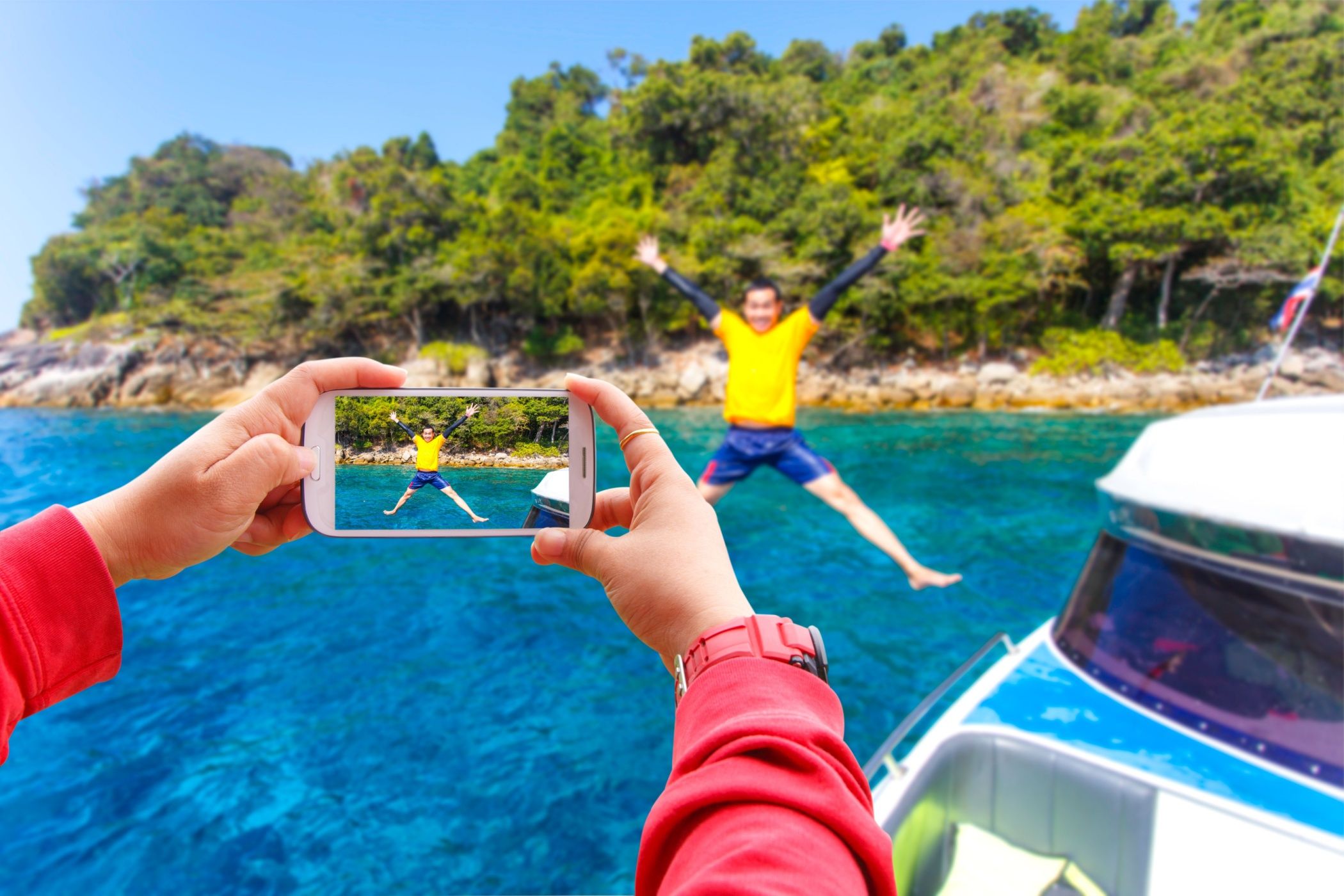 Smartphone photographing young man jumping in the water