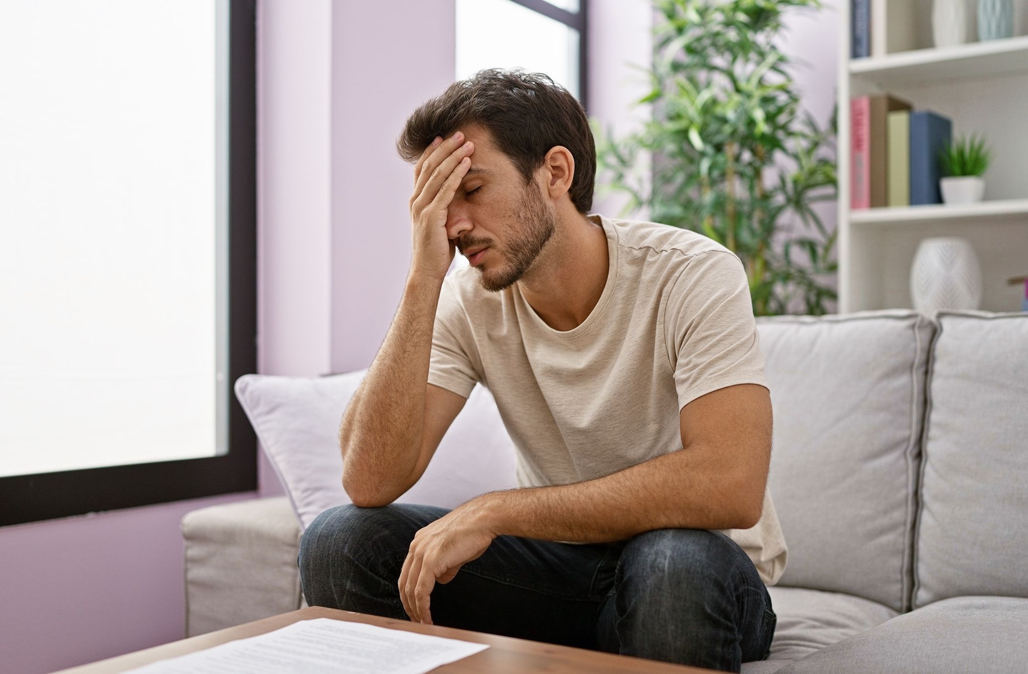 A man stressing out while sitting on a couch with a document in front of him