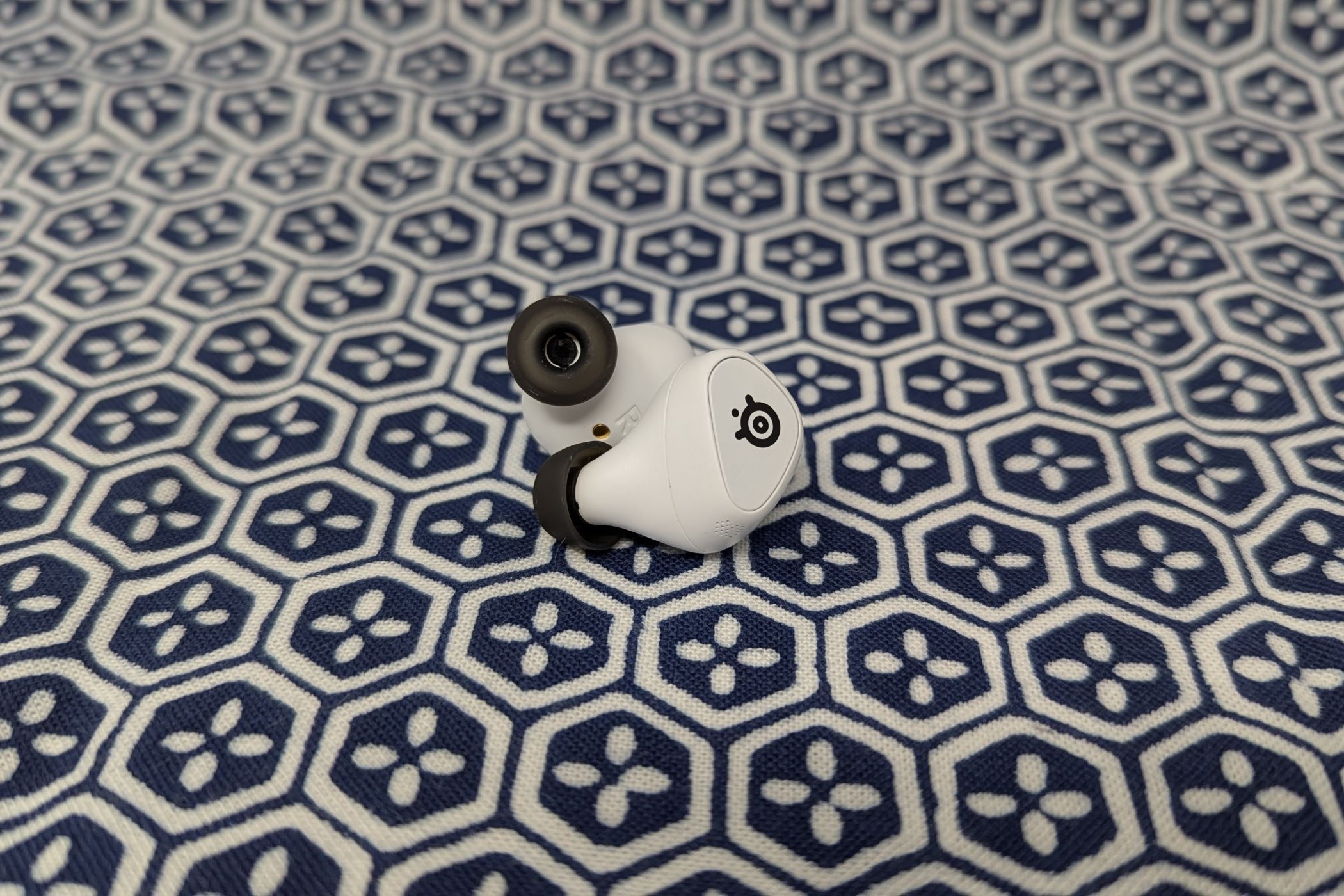 A pair of white wireless earbuds, sans case, on a blue and white cloth backgroun