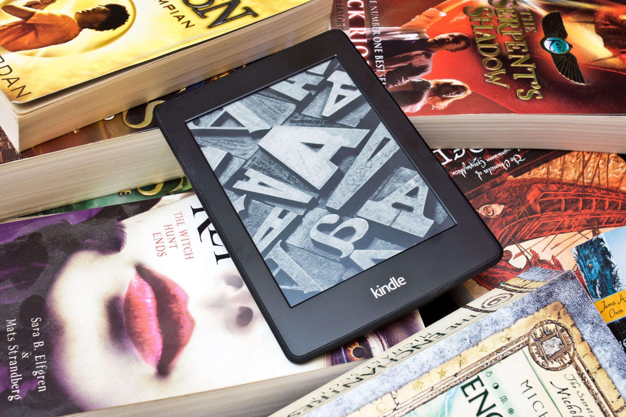 a kindle ereader on a pile of physical books