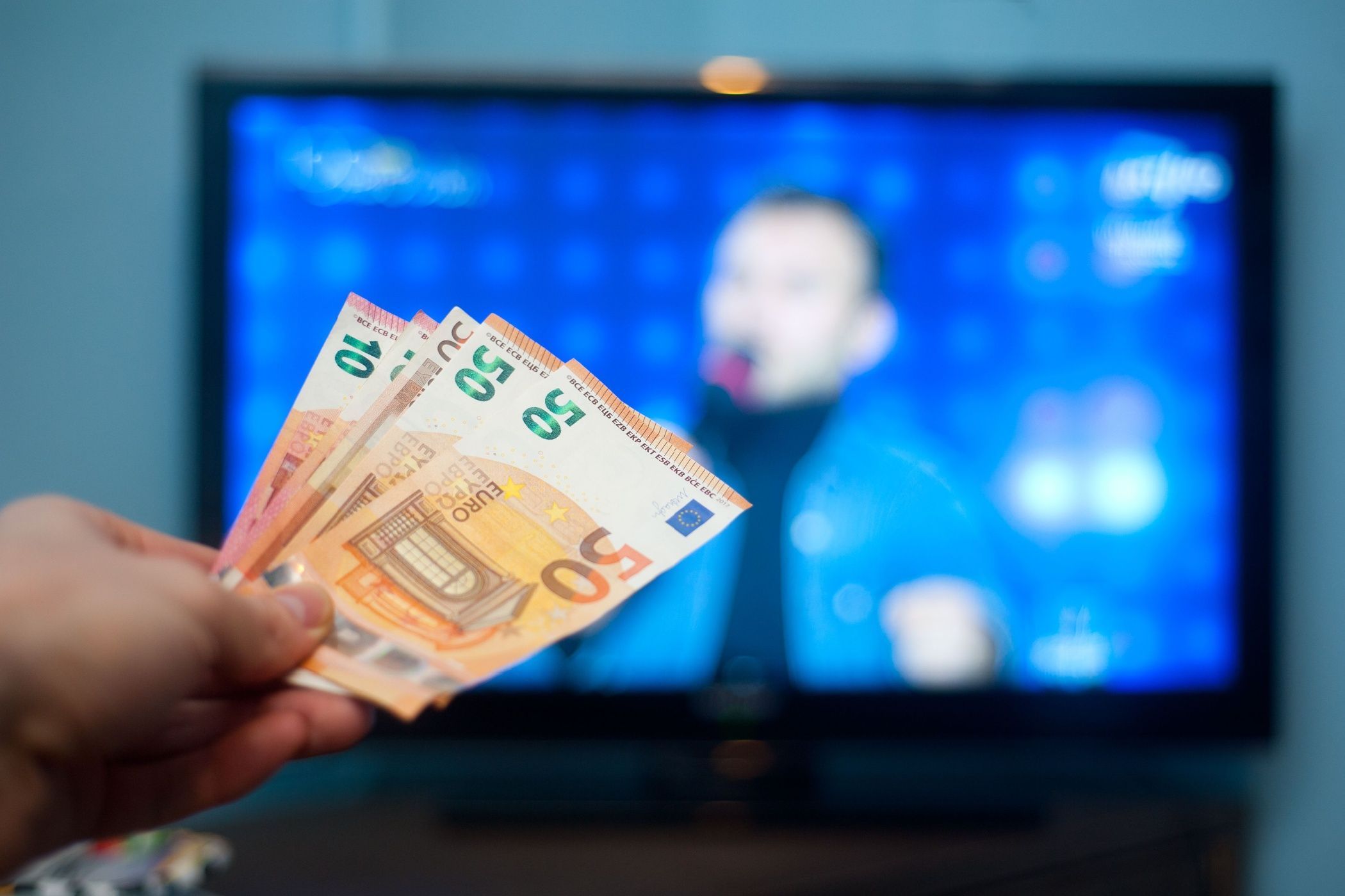 A hand holding money in front of a TV screen