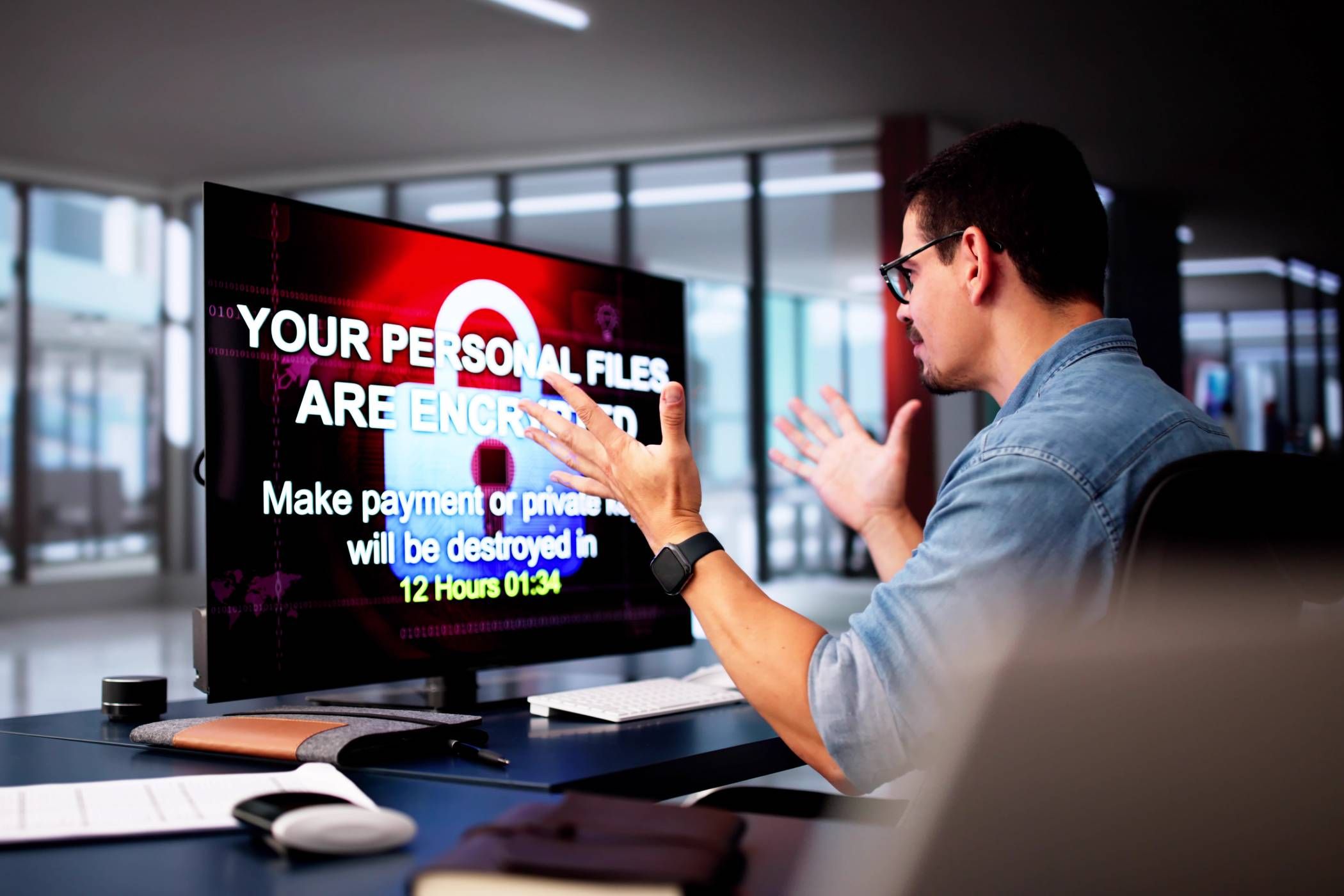 Man throwing hands up in front of monitor with ransomware message on it