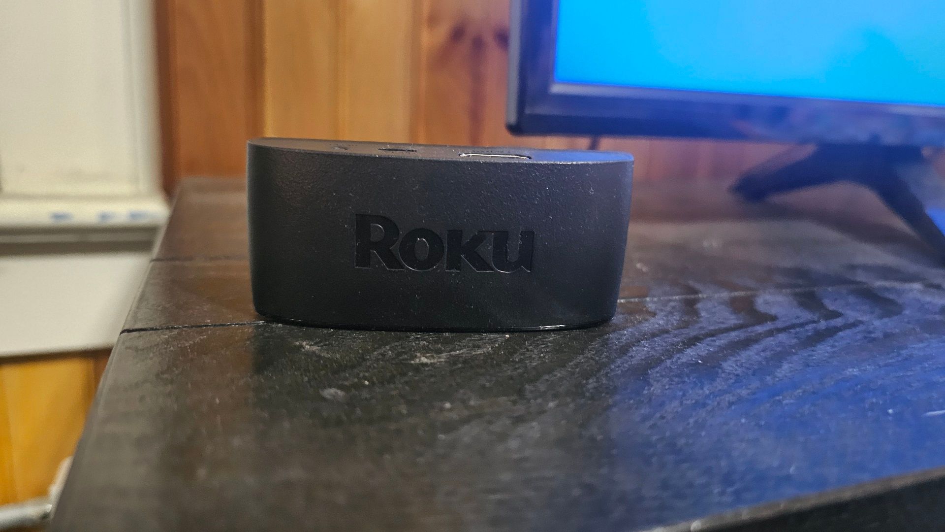 A Roku Streaming Device on top of a TV stand, next to a television.