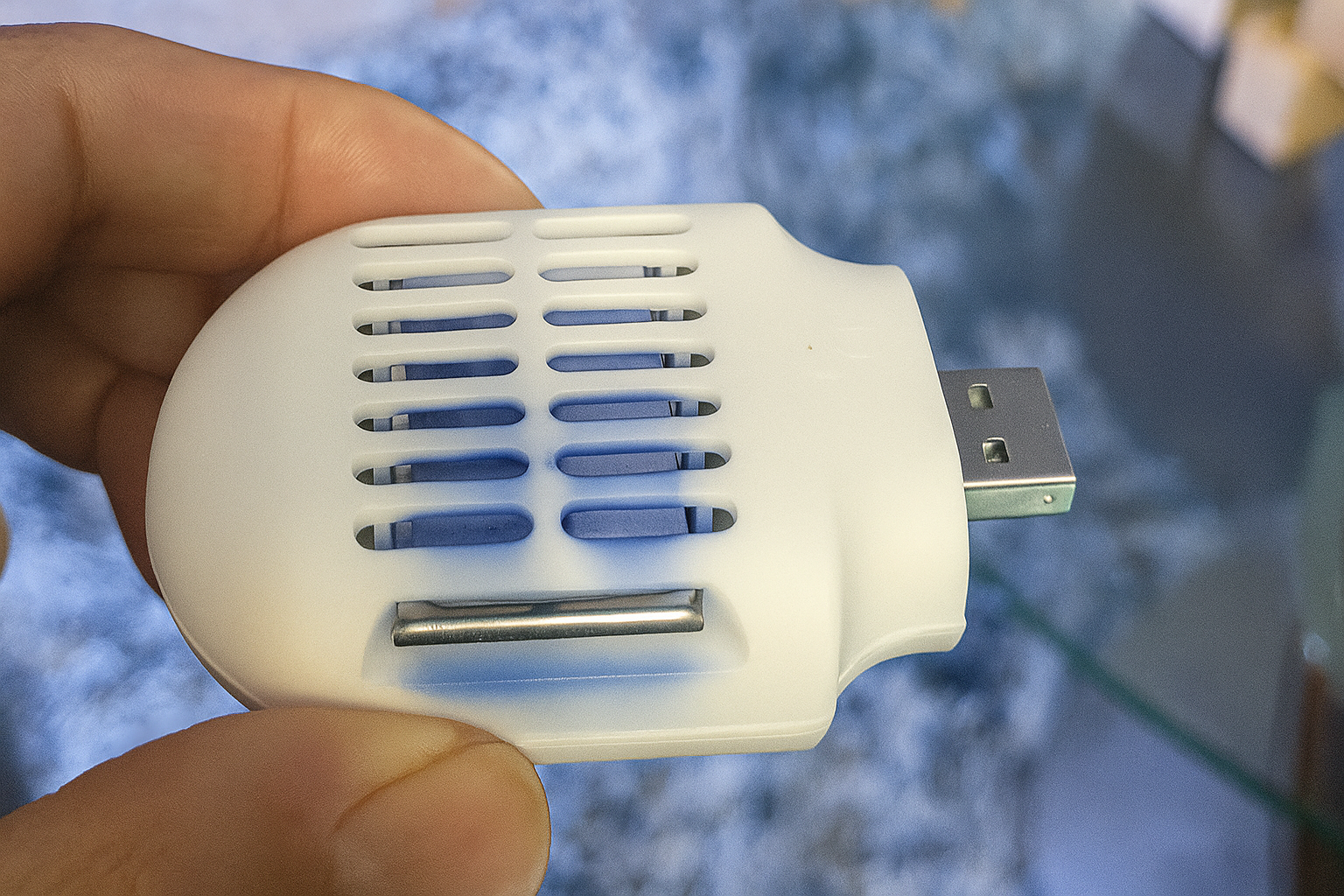 A hand holding a small, white, USB-powered mosquito repeller.