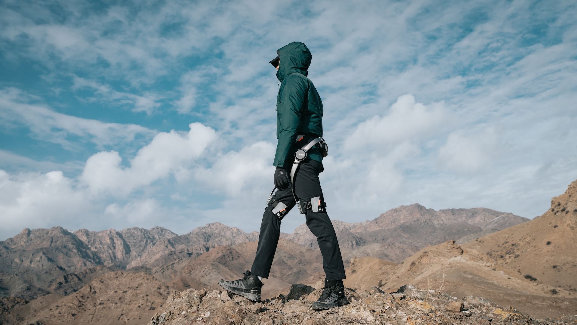 A Hypershell X user hiking over rocky mountain terrain.