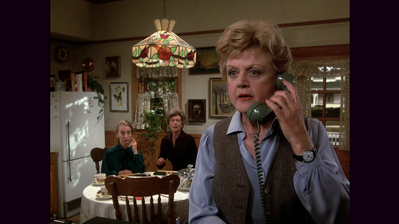 Angela Lansbury talking on the phone while two women look shocked behind her