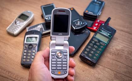 Person holding an old Sony Ericsson flip phone in front of a group of various vintage mobile phones