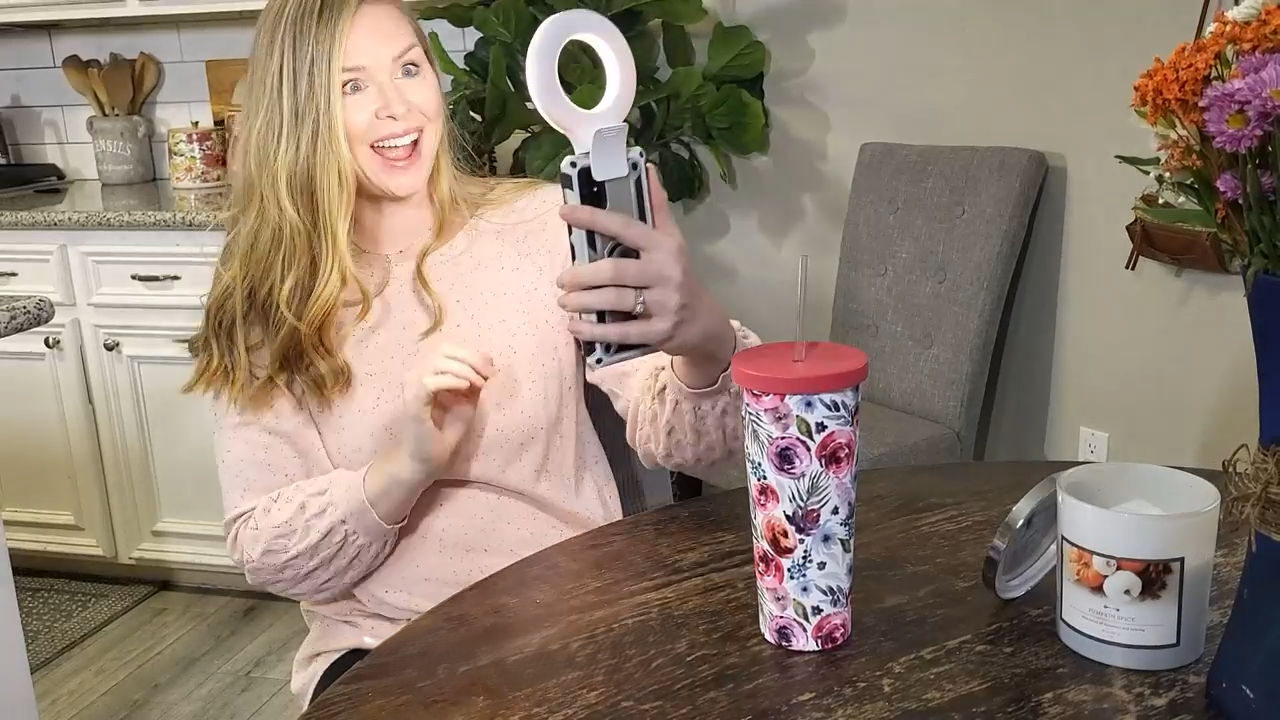 Woman sitting at a table holding a phone with ring light attached
