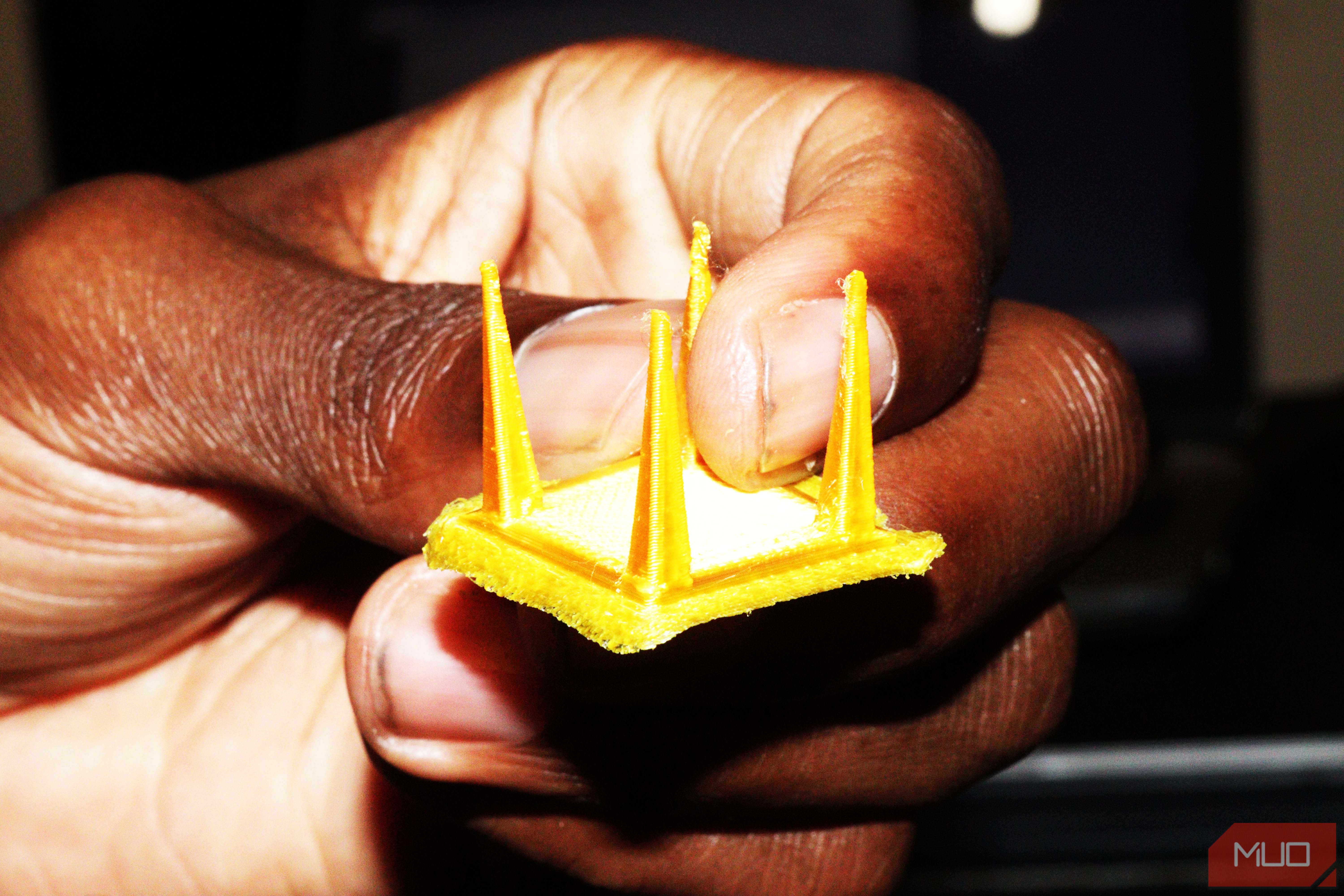 A black hand holding a yellow 3D print
