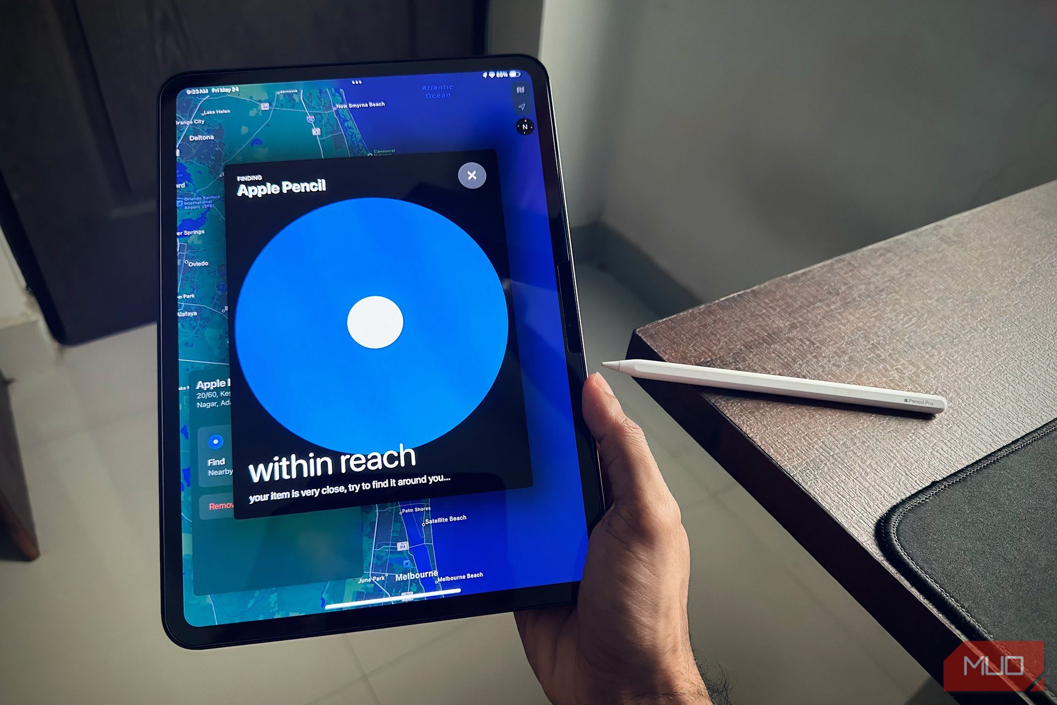 A man holding an iPad Pro using the Find My app next to an Apple Pencil Pro on a desk