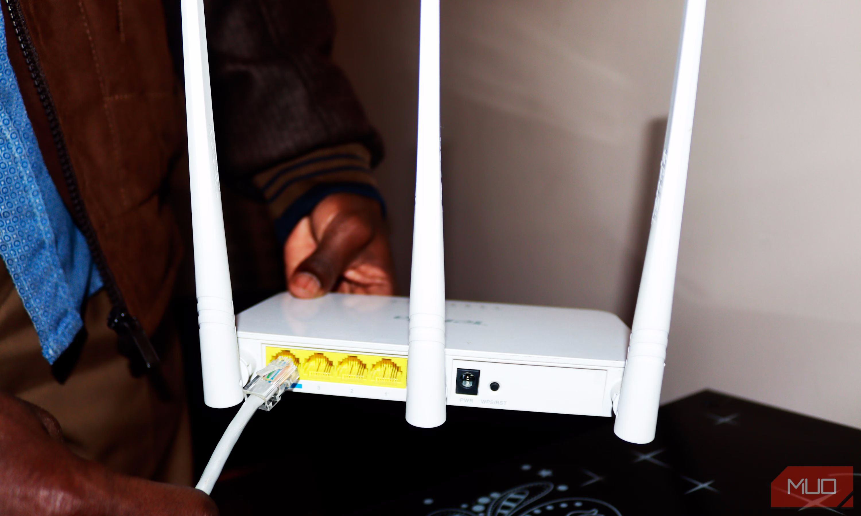 A man holding a Wi-Fi router and trying to connect an Ethernet cable