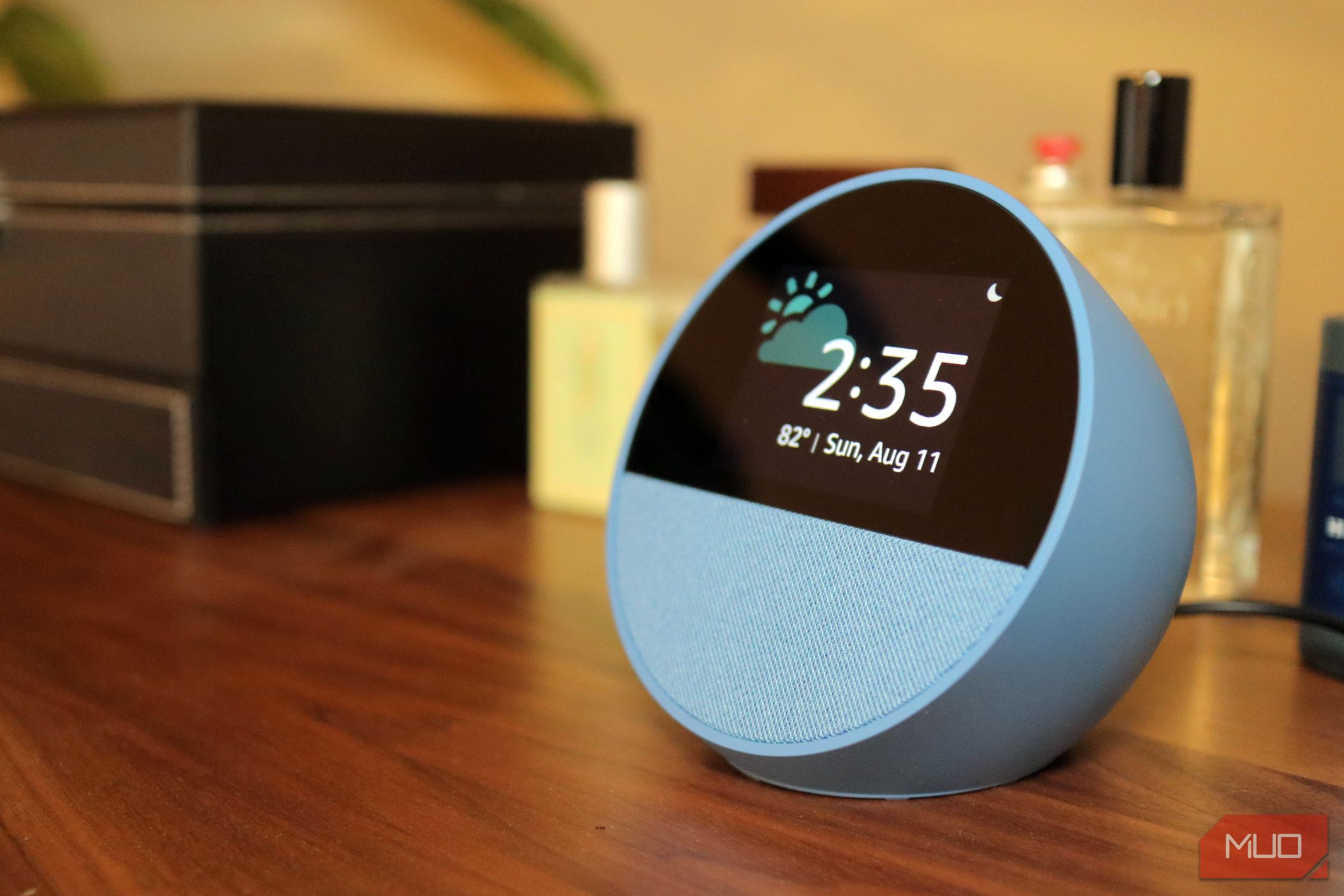 Blue Amazon Echo Spot on Wooden Dresser with Bottles and black leather case in background