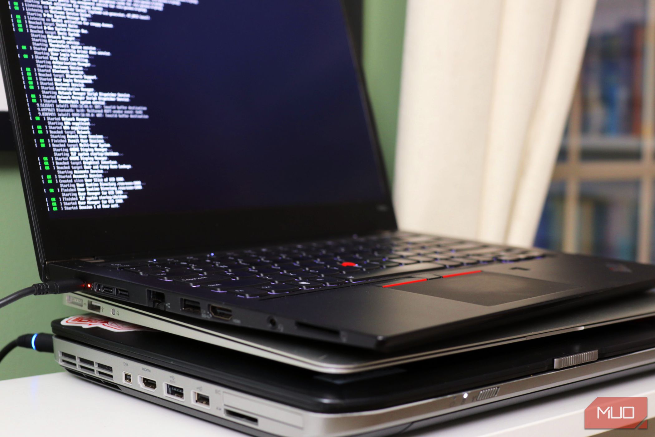 Three older laptops stacked on top of each other the top one is open and running Linux