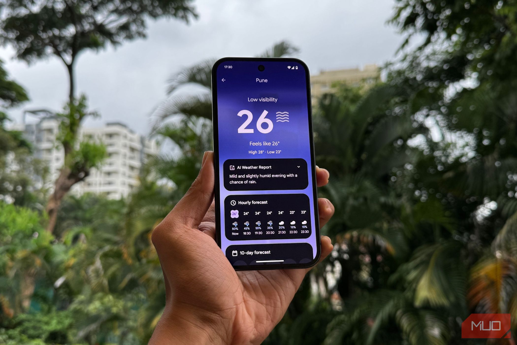 A man holding up the Pixel 9 showing the Weather app and an AI generated report