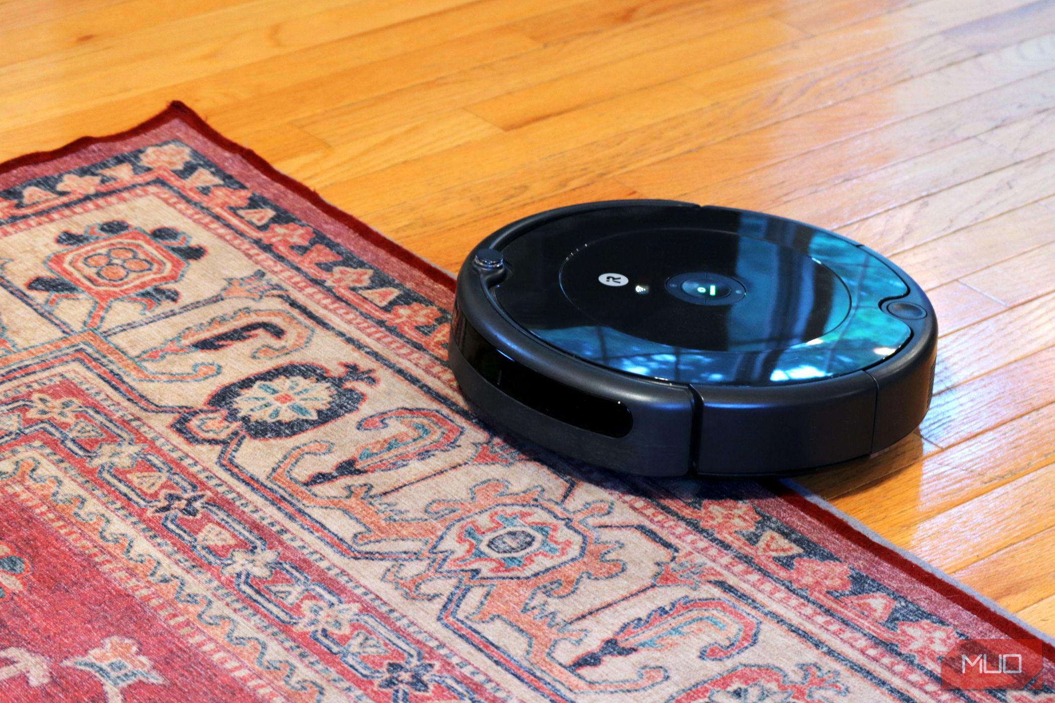 جاروبرقی هوشمند Black Roomba در نیمه راه روی فرش قرمز، با یک کف چوبی سبک در زیر آن