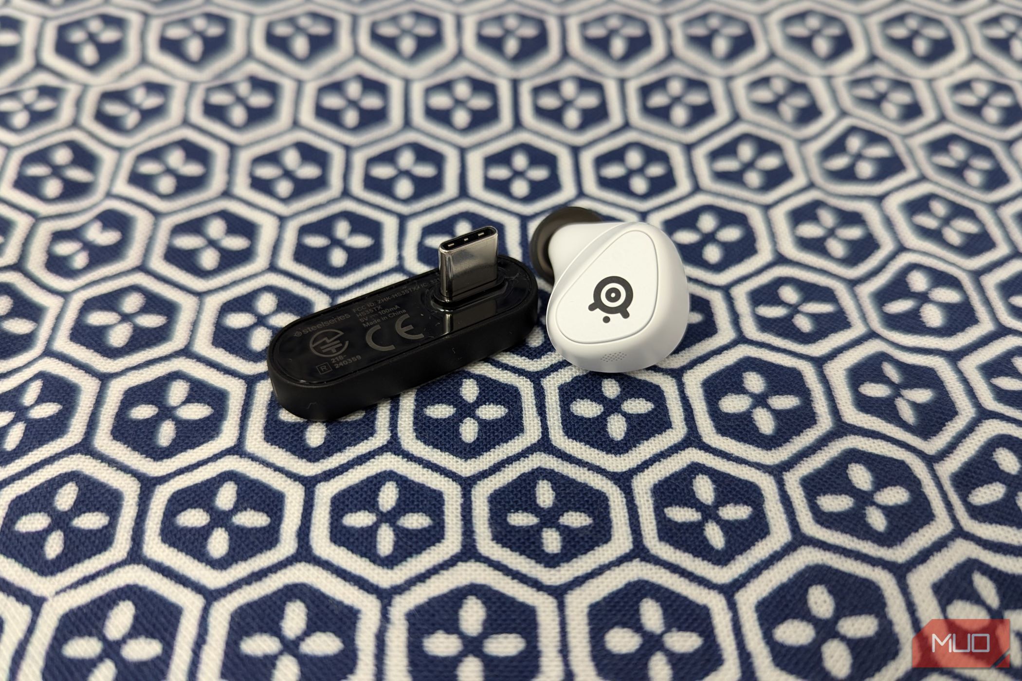 A black USB-C dongle next to a white earbud on a blue and white cloth